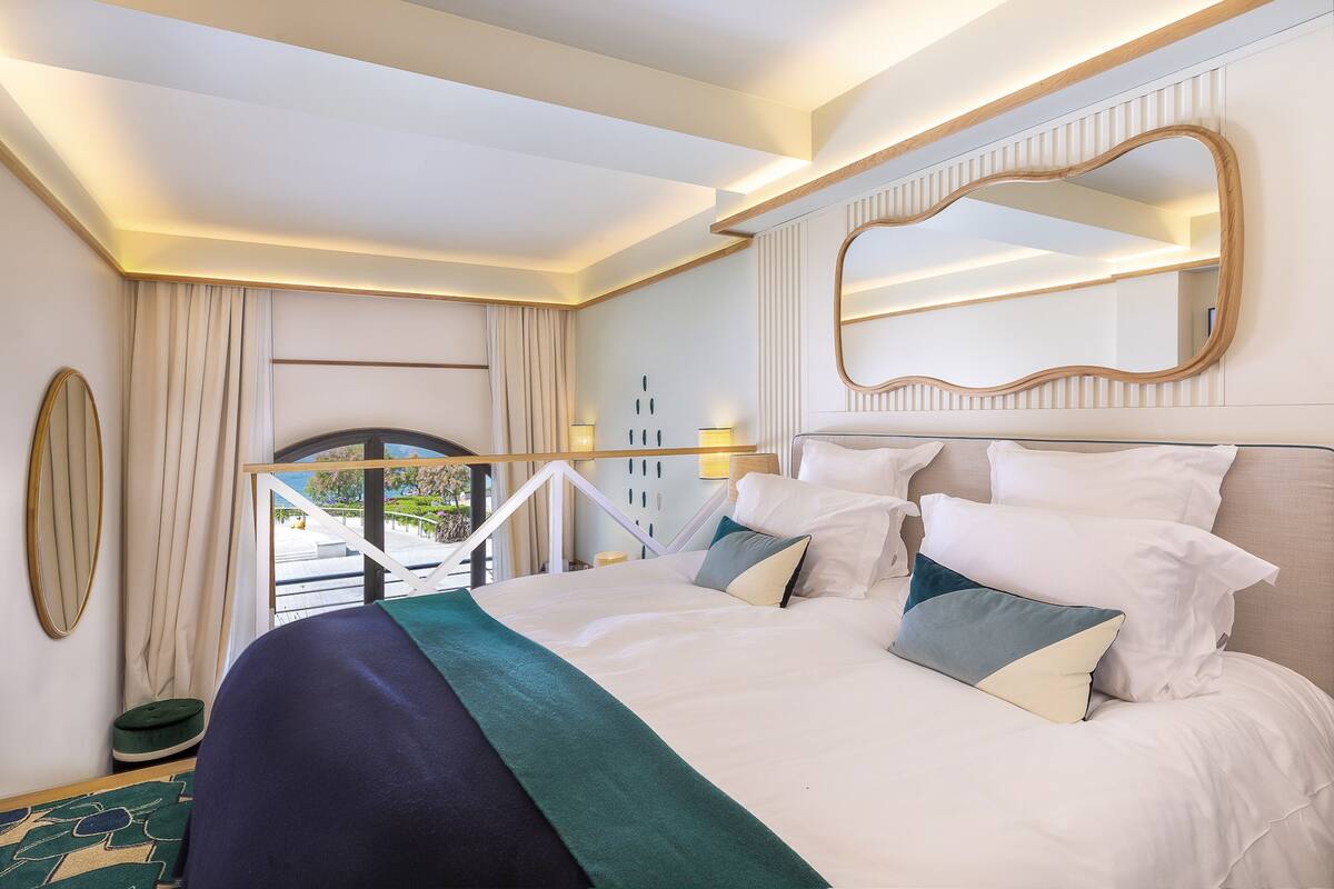 A hotel room with a large bed, a mirror, a view of the outdoors, and a balcony.
