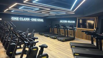 Un gimnasio con cintas de correr, elípticas y un cartel en la pared que dice 'ONE CLANN - ONE GOAL'.