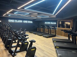 Un gimnasio con cintas de correr, elípticas y un cartel en la pared que dice 'ONE CLANN - ONE GOAL'.