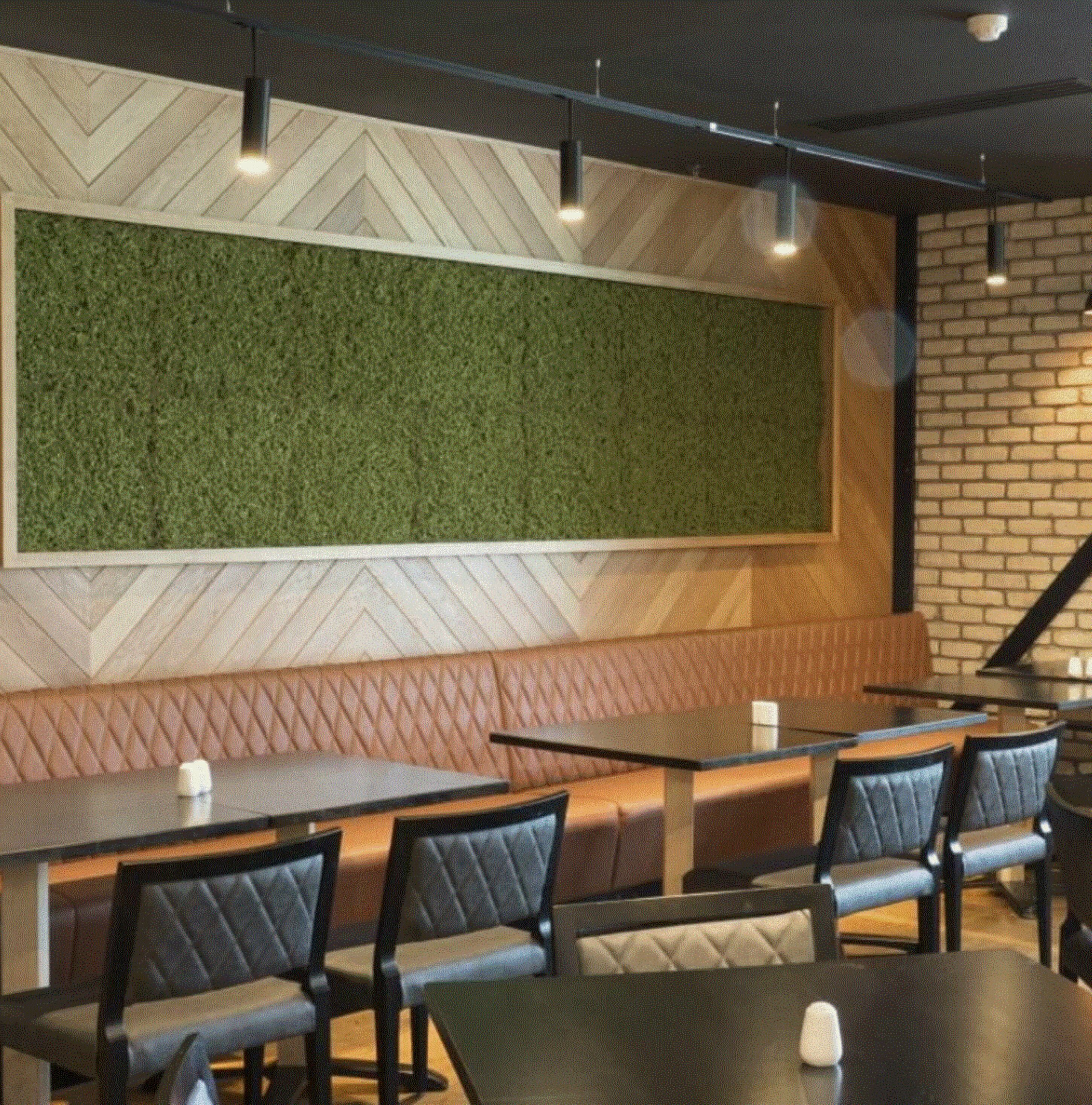 A restaurant interior with a green wall, herringbone patterned ceiling, brick wall, and a seating area with tables and chairs.