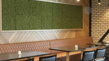 Interior de restaurante con pared verde, techo con patrón de espiga, pared de ladrillo y zona de estar con mesas y sillas.
