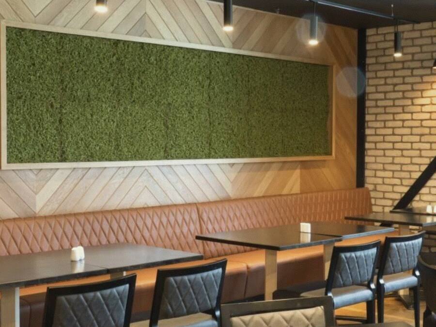 Interior de restaurante con pared verde, techo con patrón de espiga, pared de ladrillo y zona de estar con mesas y sillas.