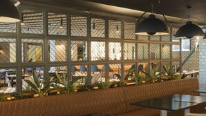 A modern restaurant with a long bench seating area, black tables, and pendant lighting. - Pillo Hotel & Leisure Club (Ashbourne)