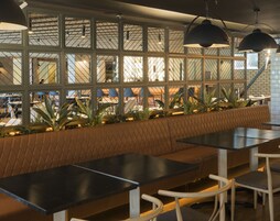Un restaurante moderno con un amplio banco para sentarse, mesas negras e iluminación colgante.