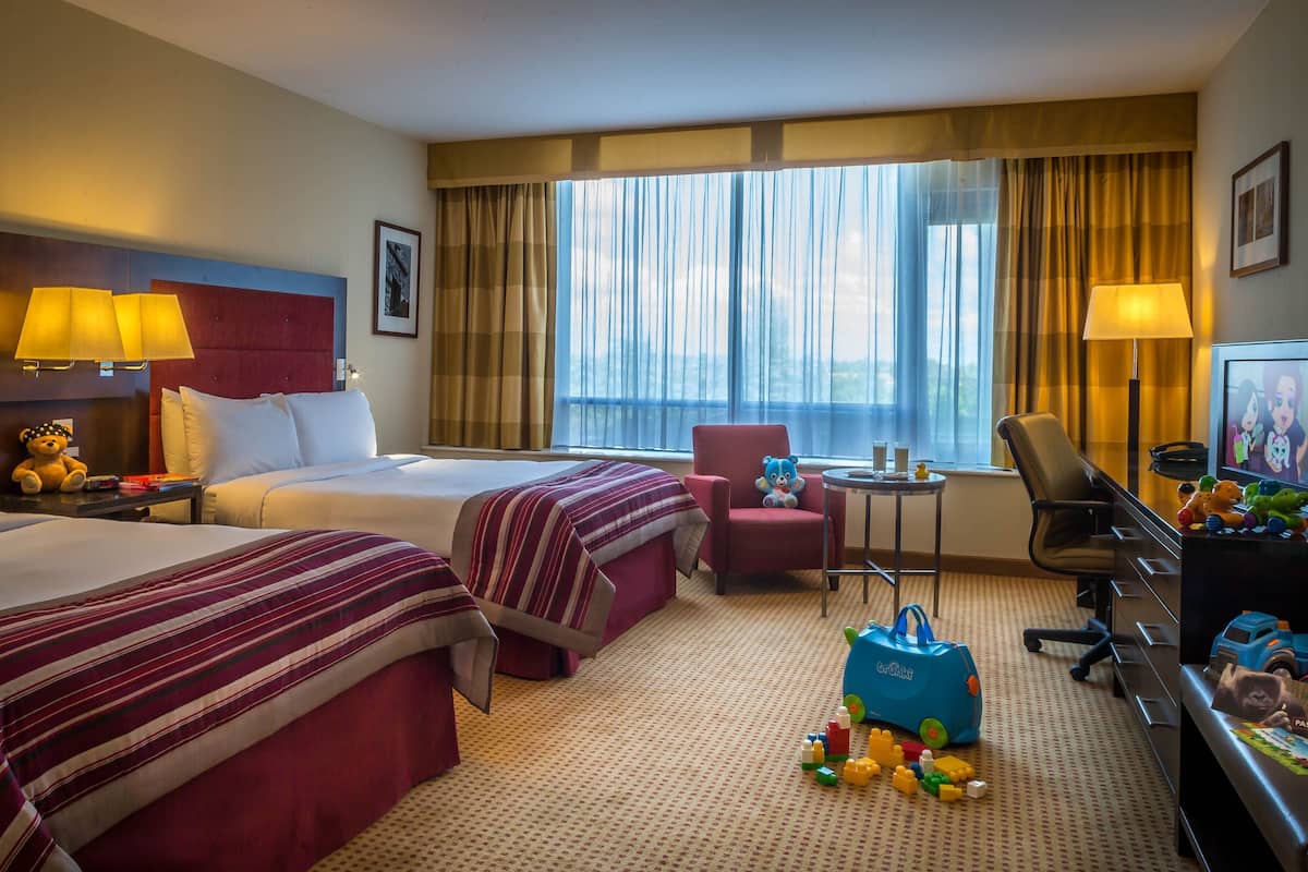 Habitación de hotel con dos camas, un escritorio, una silla, un televisor y juguetes en el suelo.