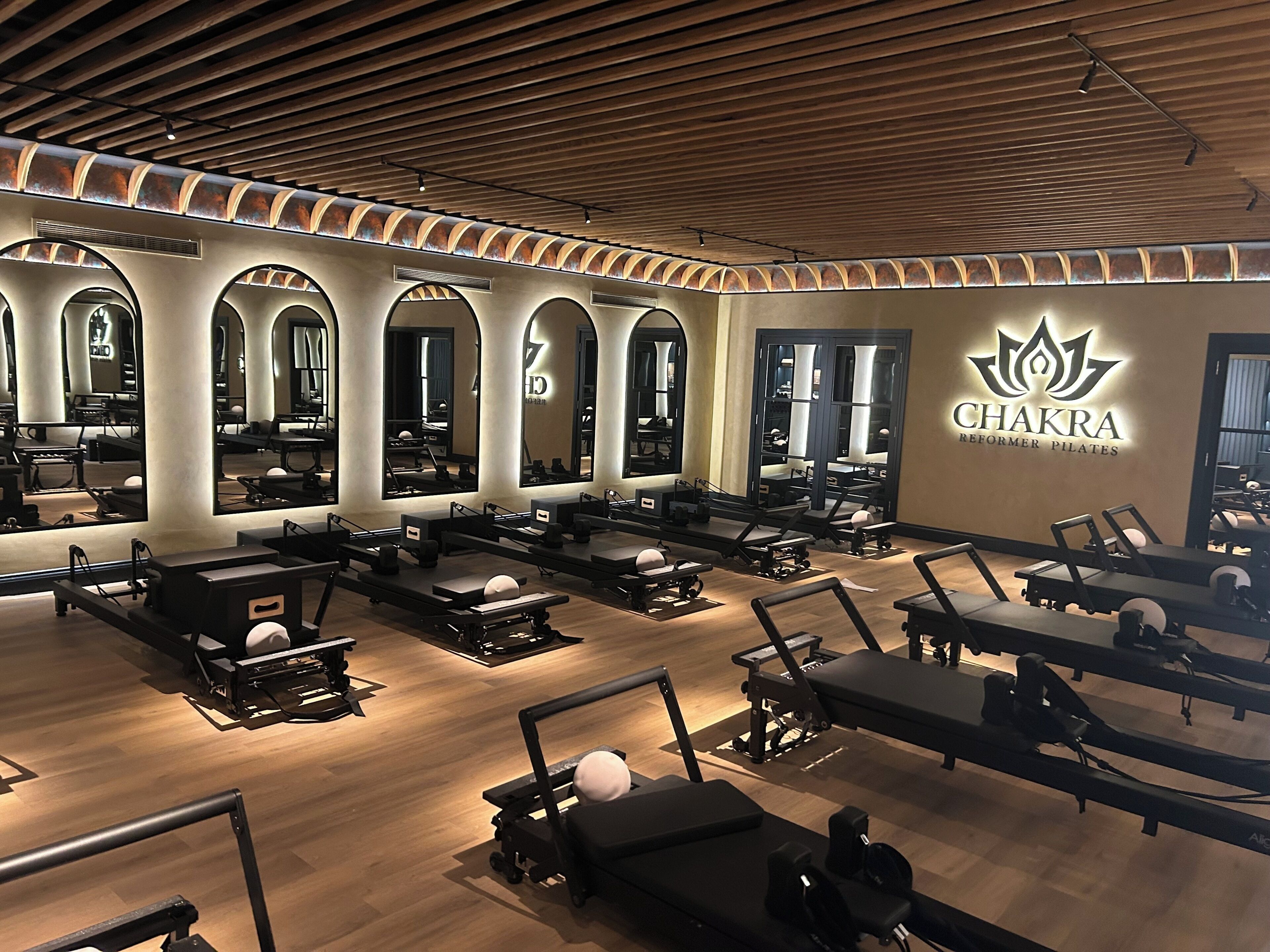 Un estudio de Pilates con paredes de espejo, suelo de madera y varias mesas de ejercicio.
