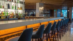 A bar area with a long counter, multiple stools, and a variety of bottles on shelves. - Pillo Hotel & Leisure Club (Ashbourne)