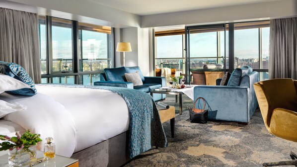 Habitación de hotel con una cama grande, un sofá, una mesa de comedor y vistas a la ciudad.