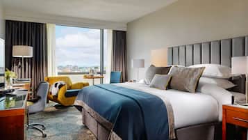 Una habitación de hotel con una cama grande, un escritorio con silla, una ventana con cortinas y vista a la ciudad.