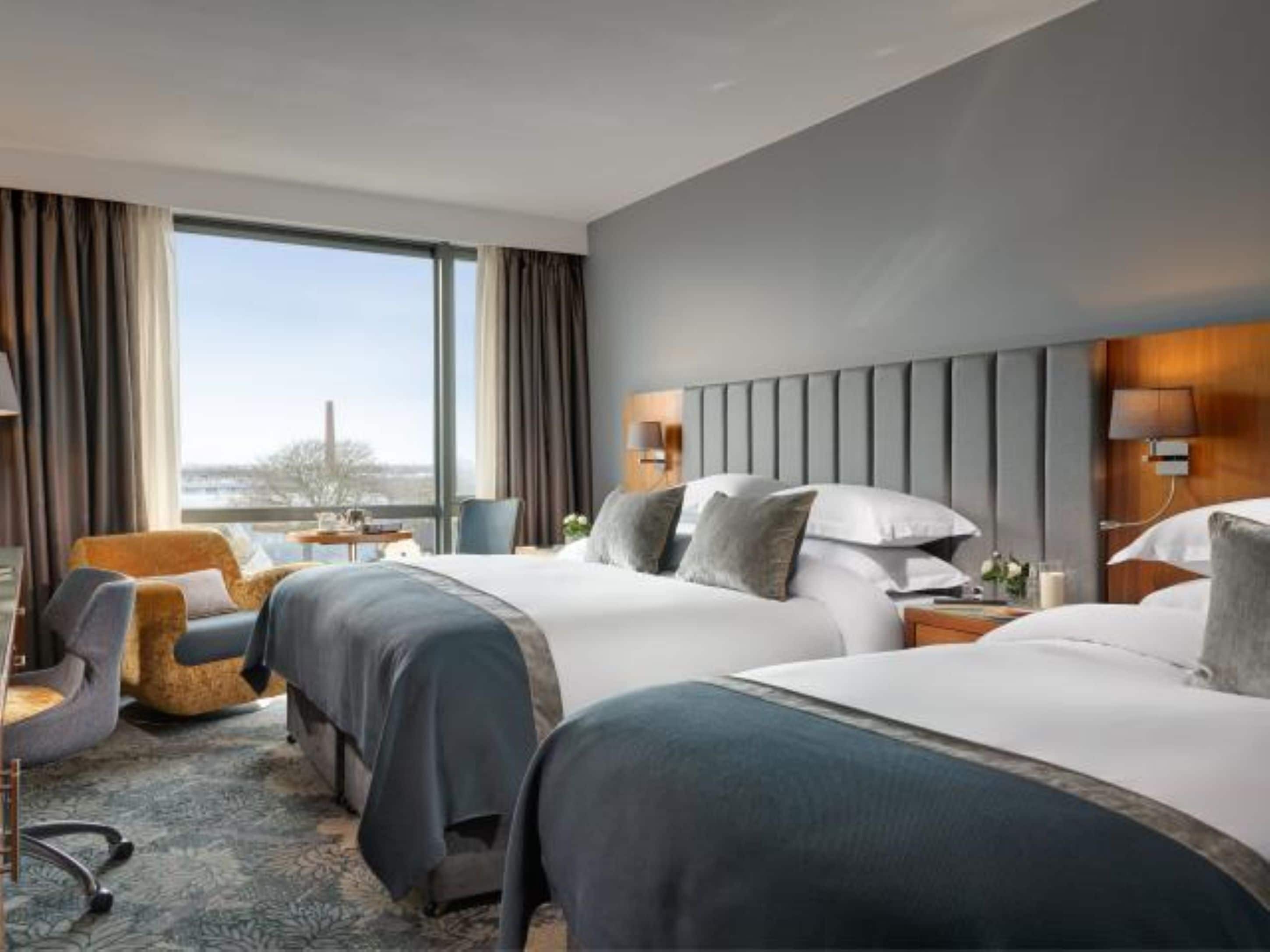 A hotel room with two beds, a view of the city, and a large window.
