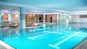 Un'ampia piscina interna con acqua cristallina, circondata da sdraio e un muro in legno.