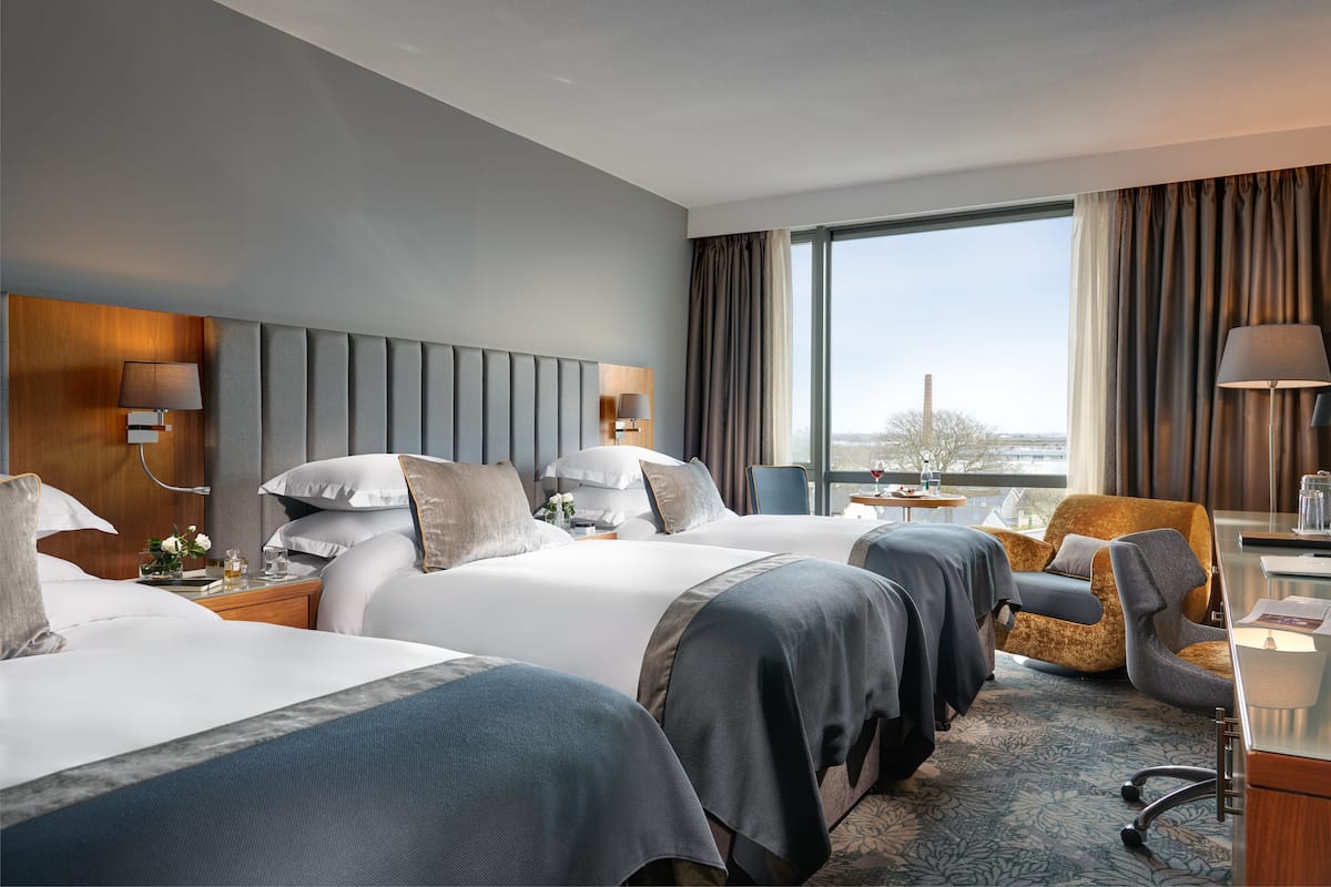 A hotel room with two beds, a desk, a chair, and a large window offering a view.