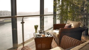 Un balcone con mobili in vimini, un vassoio con tè e pasticcini, e vista su un fiume e degli edifici.