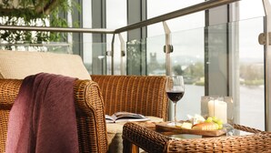 Un divano in vimini con una coperta viola, un bicchiere di vino rosso, una candela e un tagliere con uva.