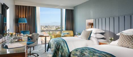 Habitación de hotel con una cama grande, un escritorio con silla, una lámpara y vistas a la ciudad.
