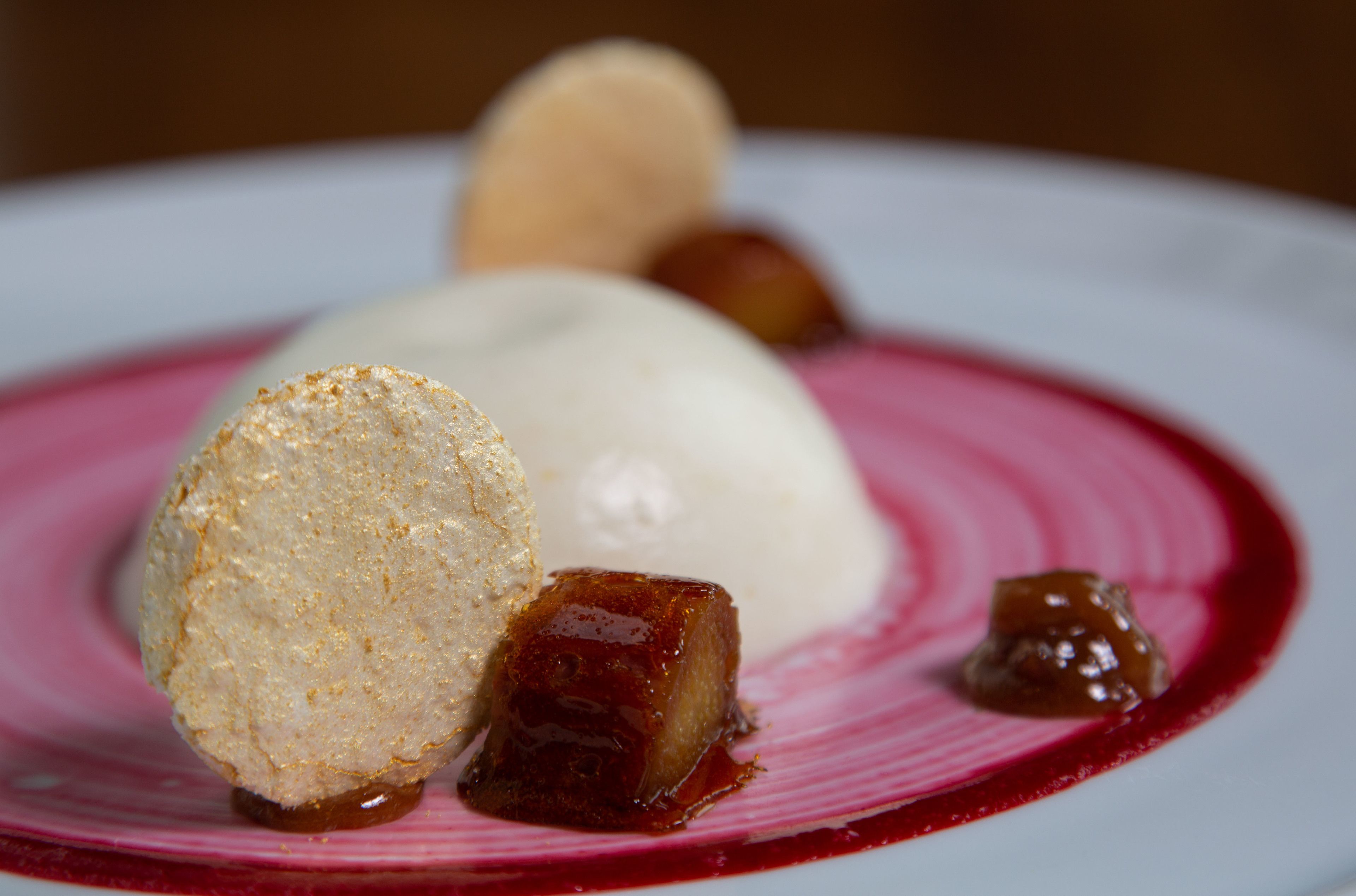 Un plato de postre con una bola de helado, una fruta caramelizada y un pastel redondo sobre un plato rosa.