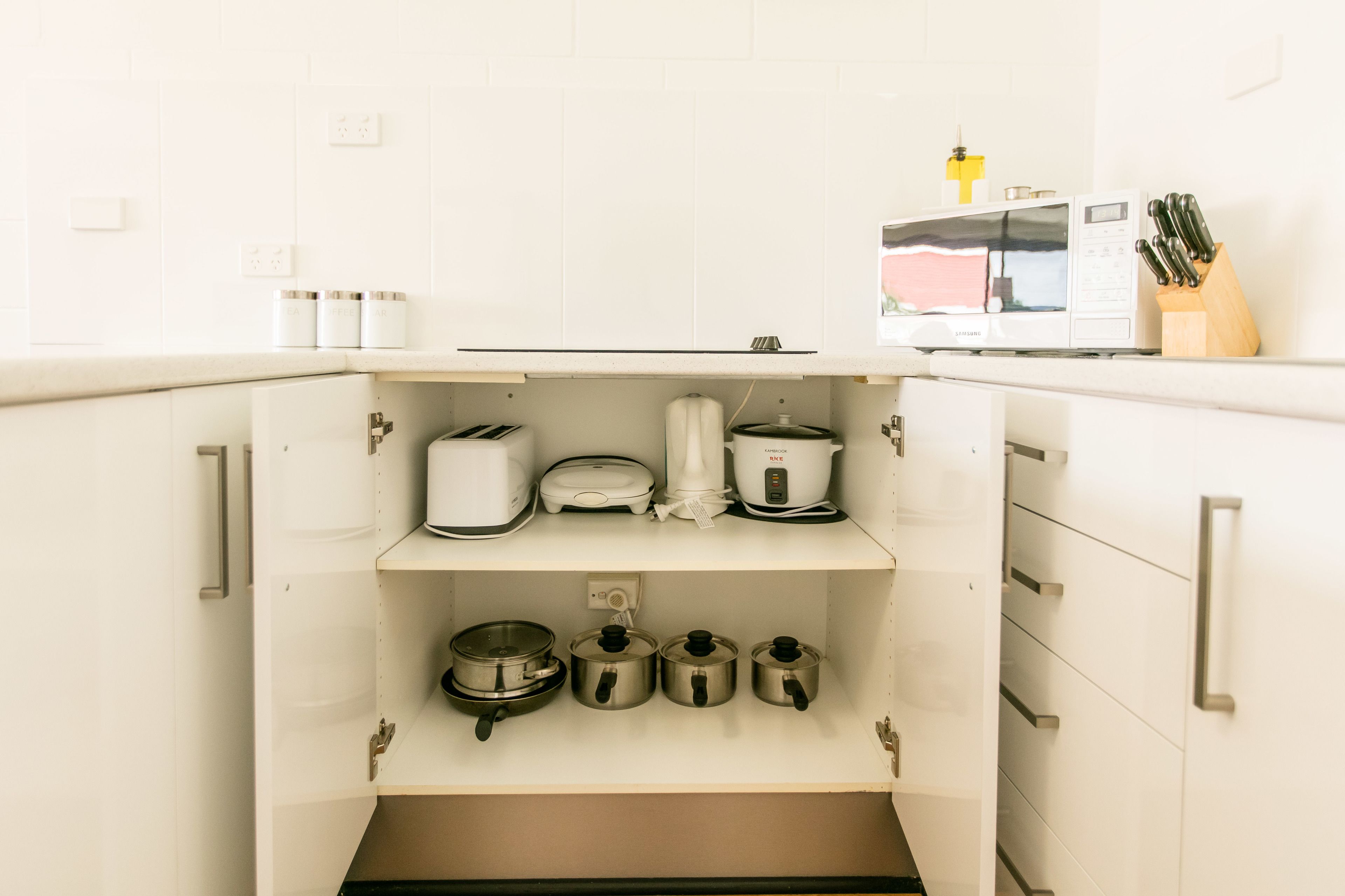 Una cocina con gabinetes blancos, microondas, tostadora y cafetera sobre la encimera.