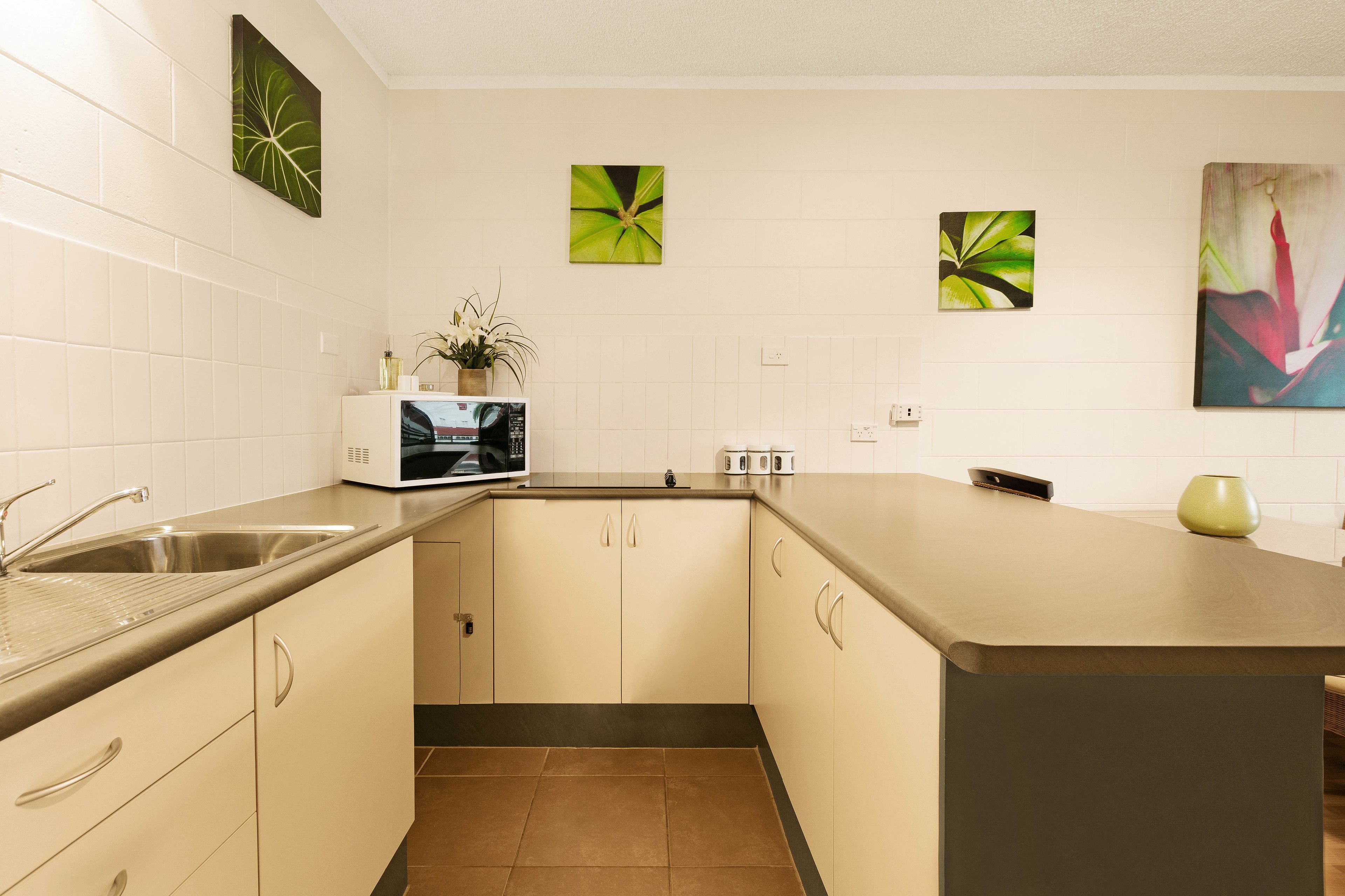 A modern kitchen with white cabinets, a stainless steel sink, a microwave, and a small island with a green vase.