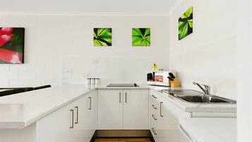 A modern kitchen with white cabinets, a stainless steel sink, and a microwave. There are three green leaf paintings on the wall.