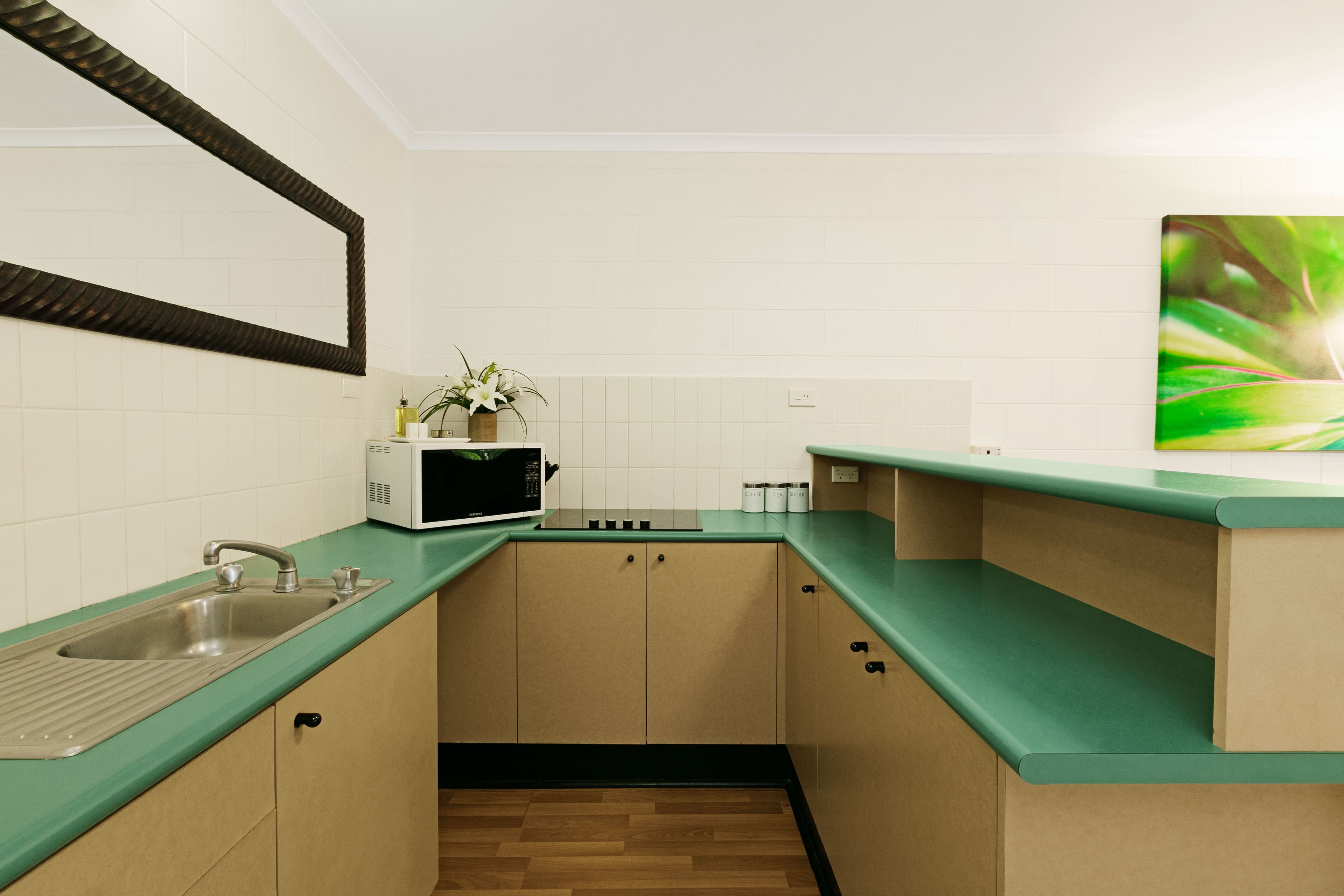 A modern kitchen with a green countertop, stainless steel sink, and wooden cabinets.