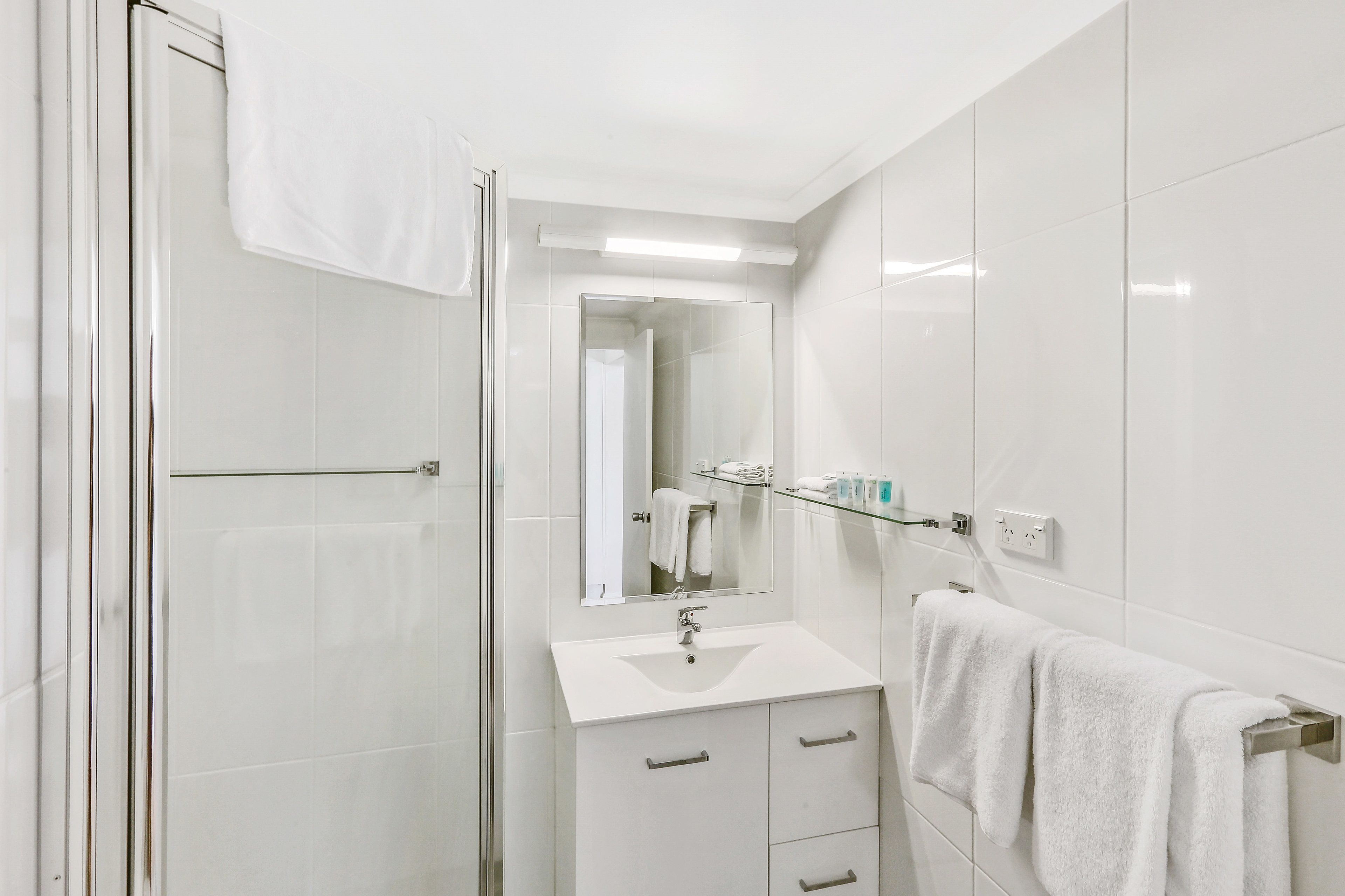 A modern bathroom with a glass shower enclosure, a white sink, and a mirror above it.