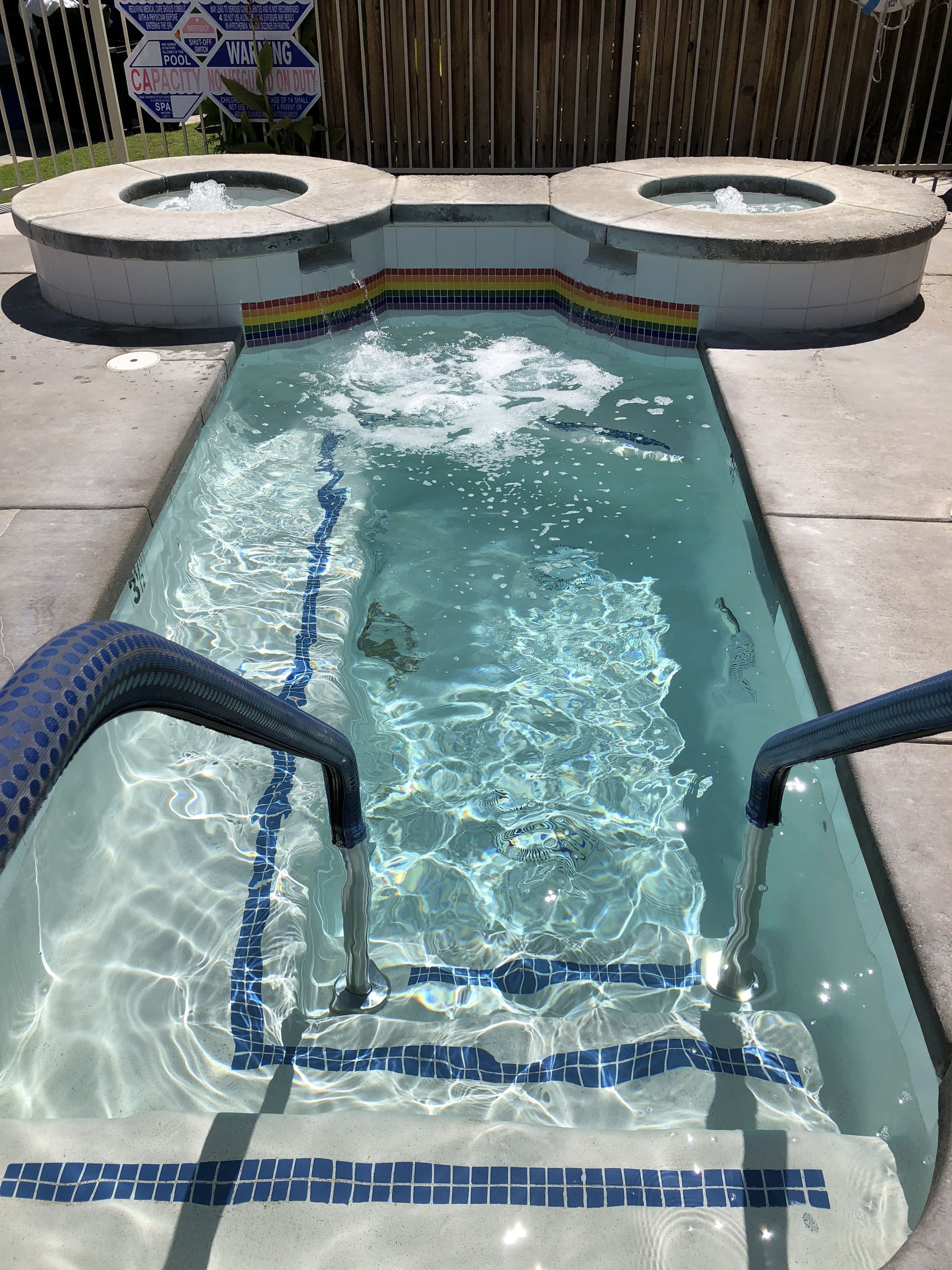 En rektangulär pool med klart vatten, blå mosaikplattor och två hoppbrädor.
