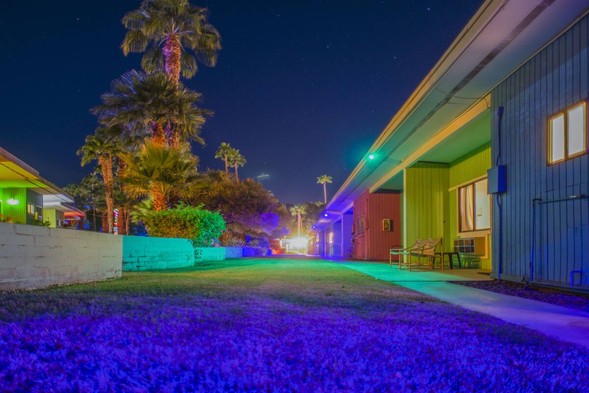 A hotel with a well-lit driveway, palm trees, and a clear night sky.