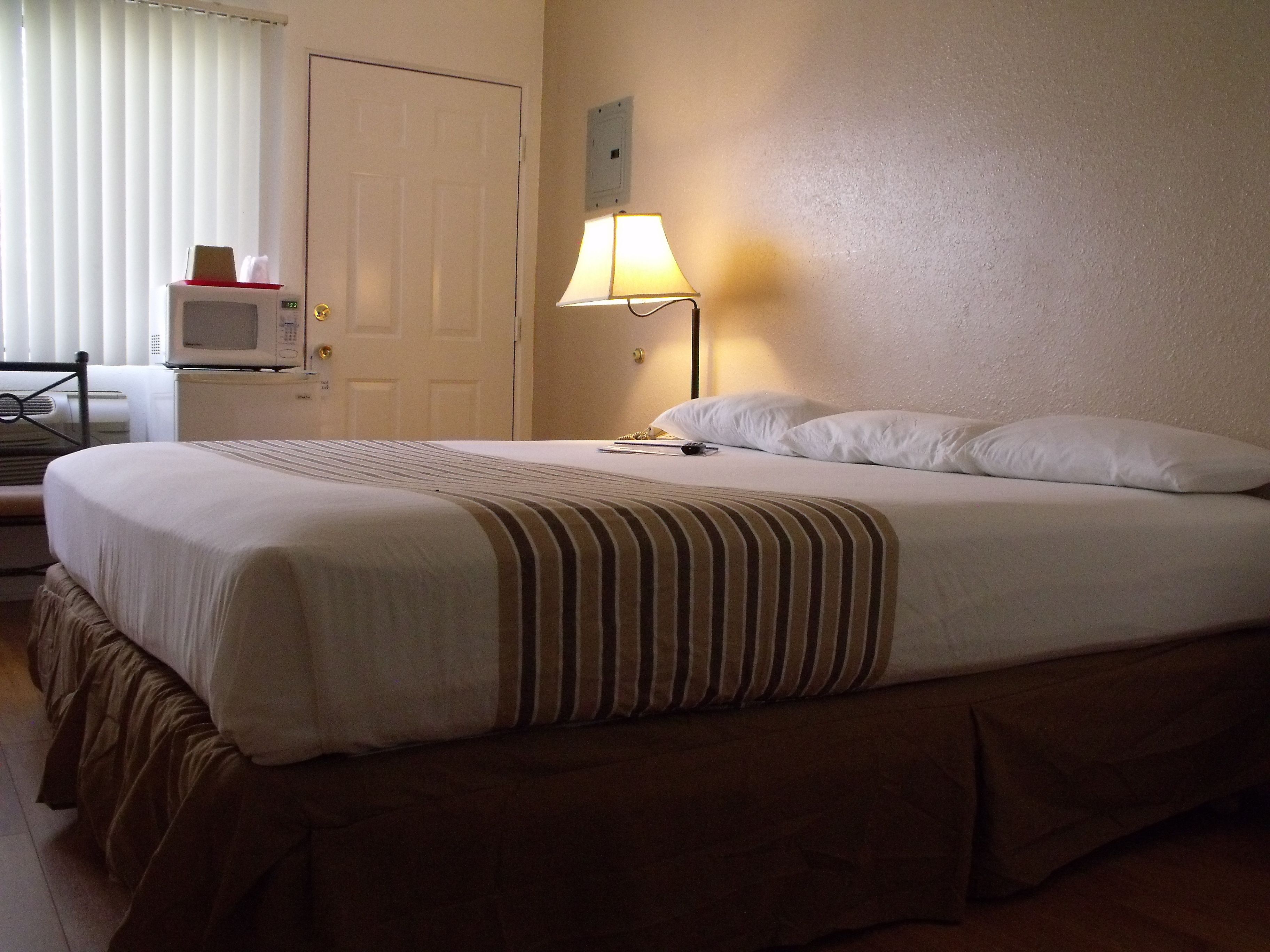 A hotel room with a single bed, a bedside lamp, a television, and a door.