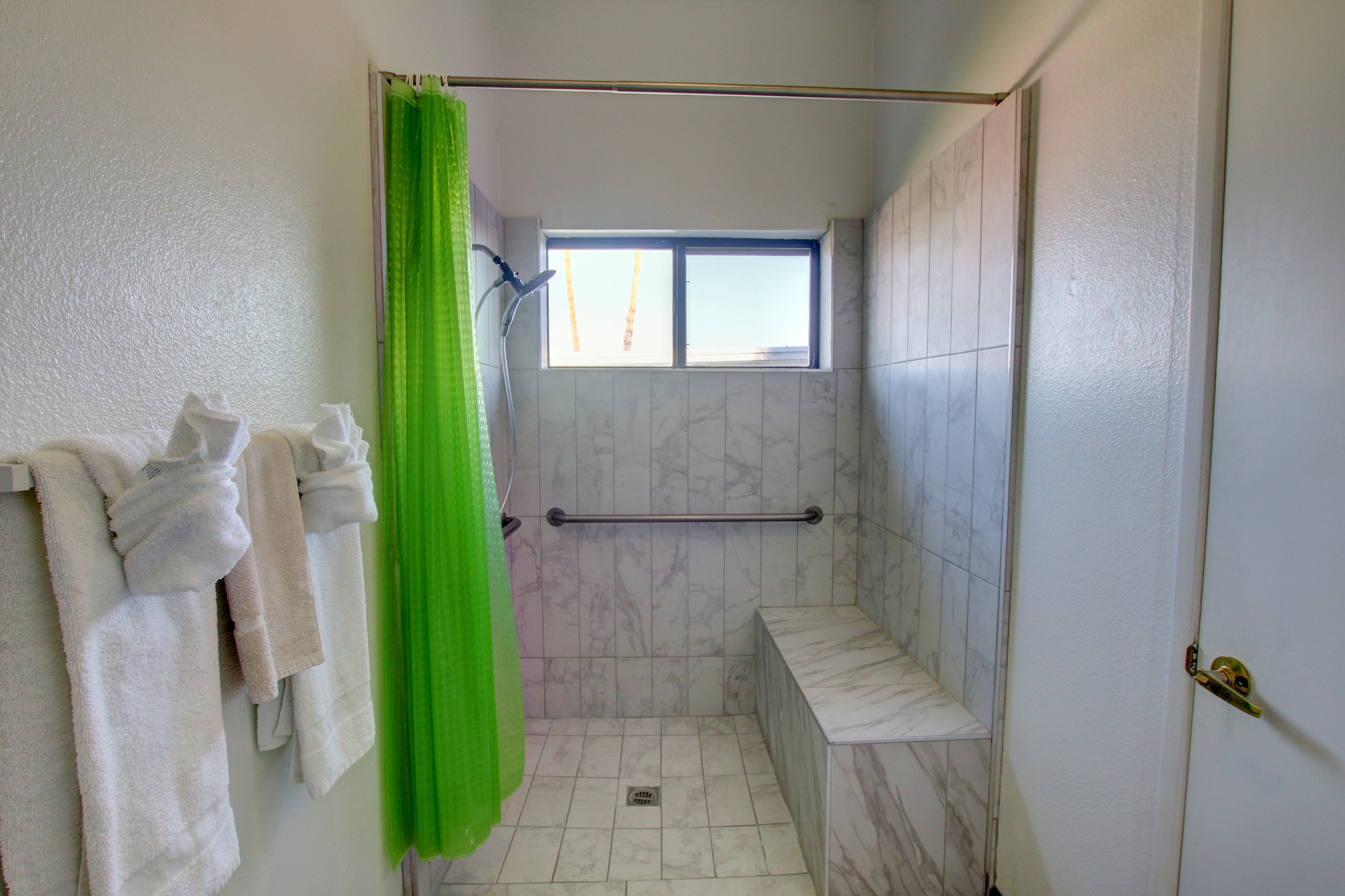 A bathroom with a shower, a window, and a towel rack with towels.
