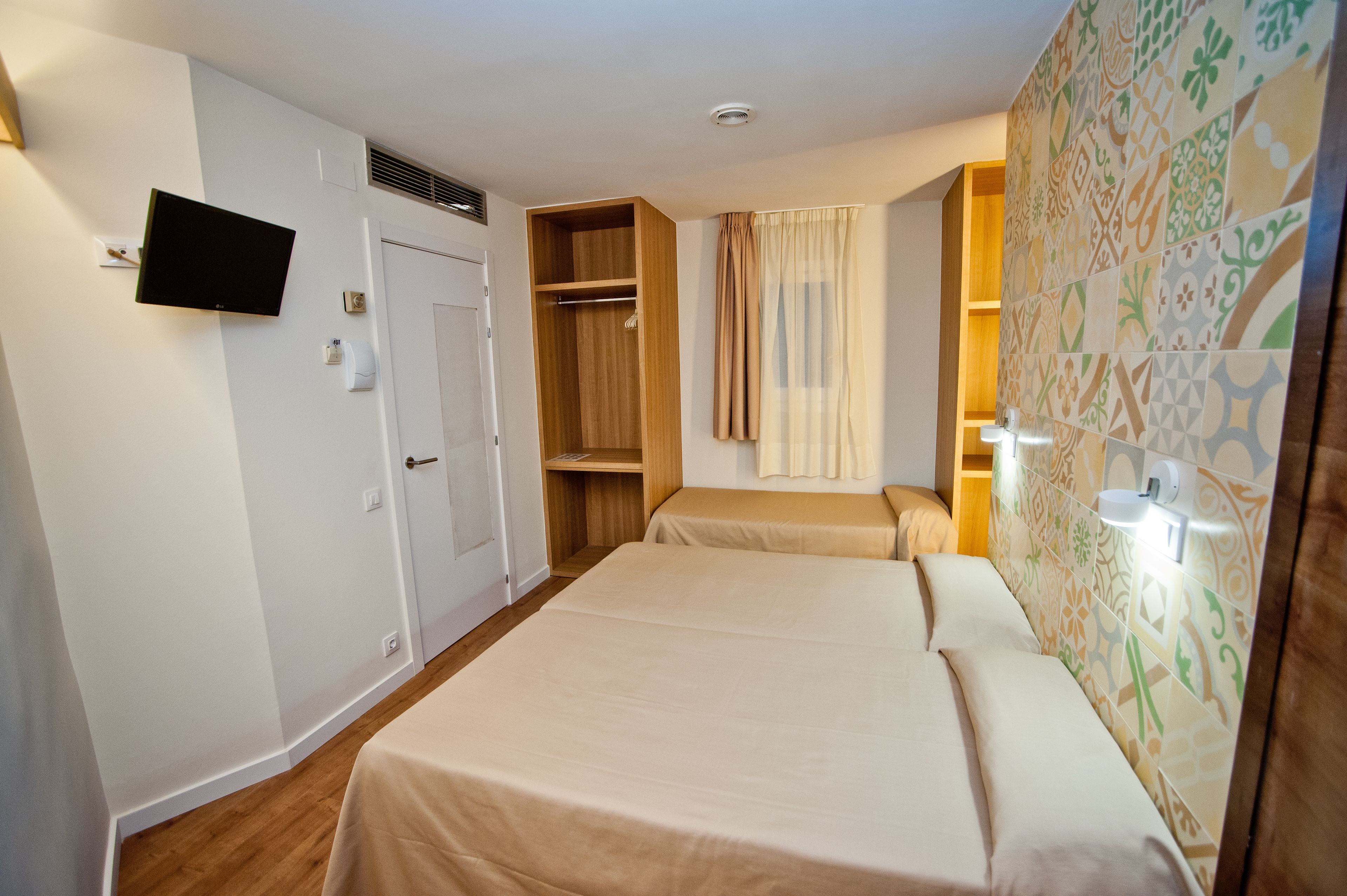 Habitació d'hotel amb llit, televisió penjada a la paret, armari i bany amb cortina de dutxa.