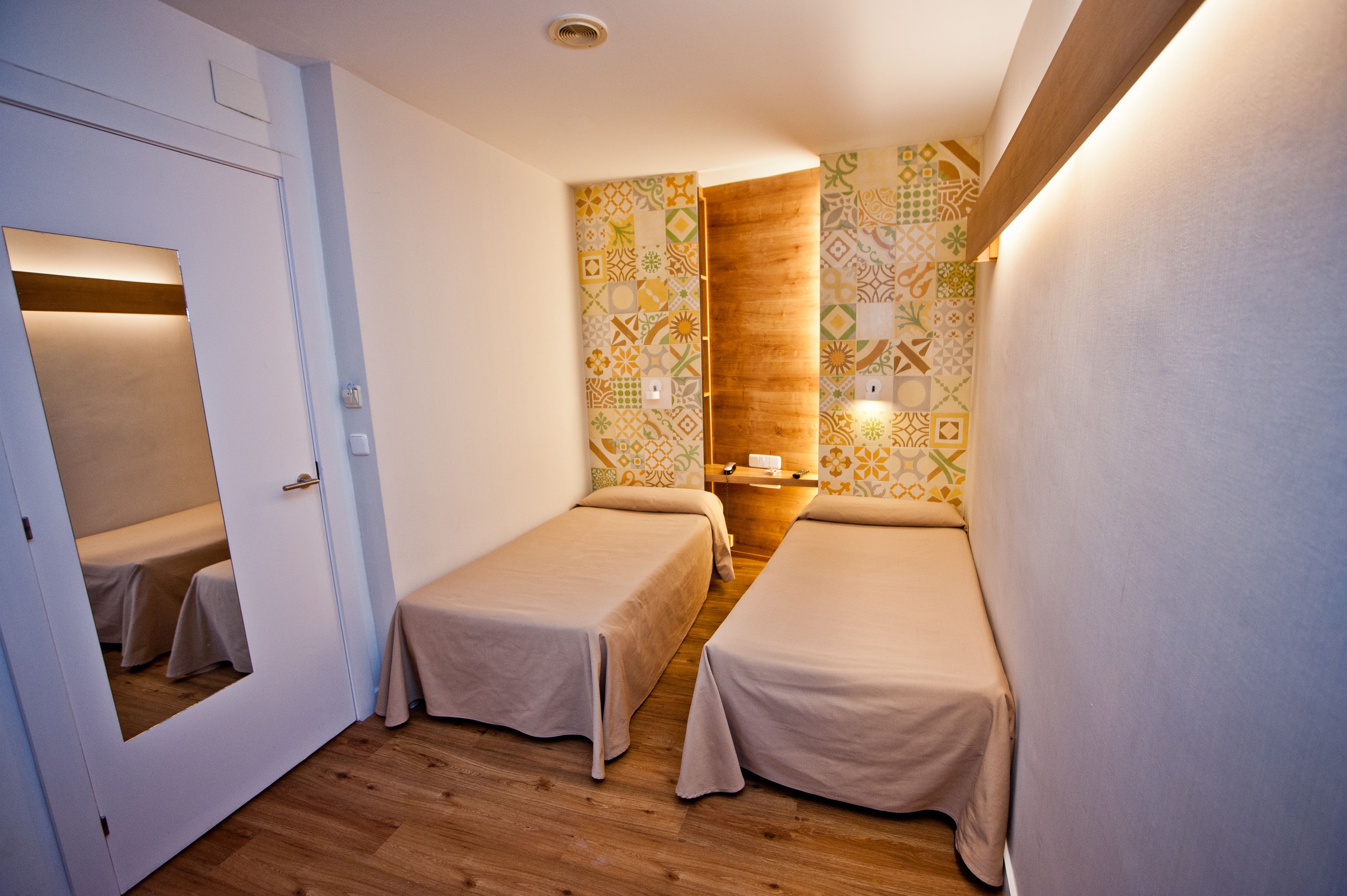 Una habitación pequeña y bien iluminada con dos camas individuales, un panel de madera decorativo y papel tapiz estampado.