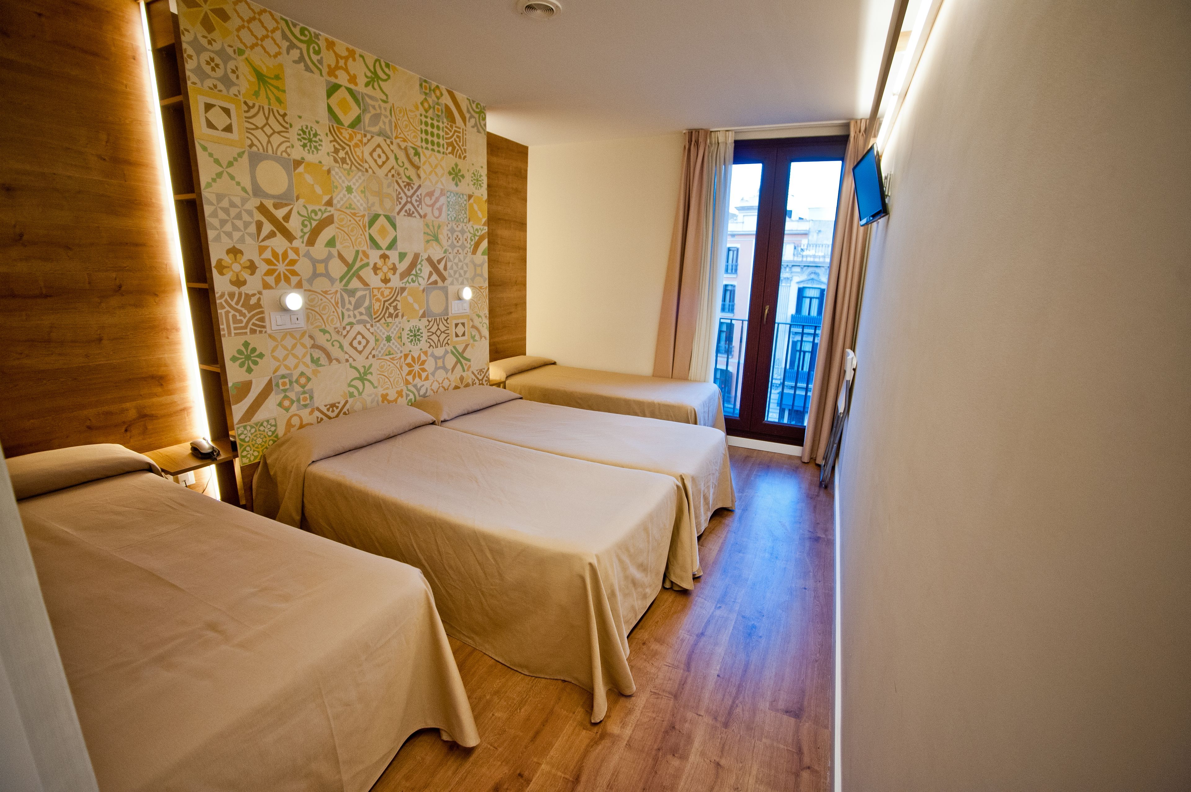 A hotel room with two single beds, a wooden headboard, a patterned wall, and a balcony with a view.