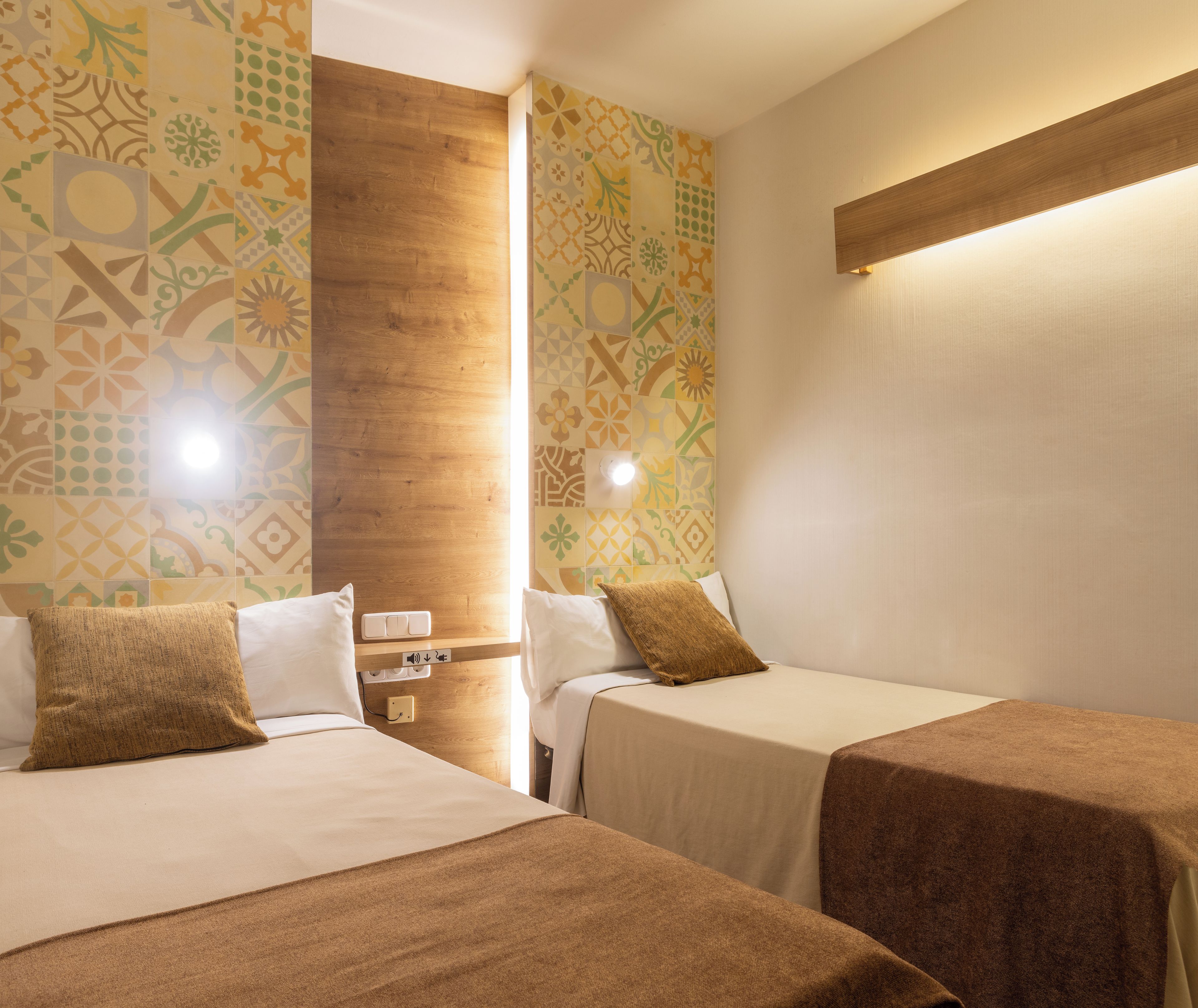 Habitación de hotel con dos camas, una pared de acento de madera, papel tapiz estampado y una mesita de noche con lámpara.