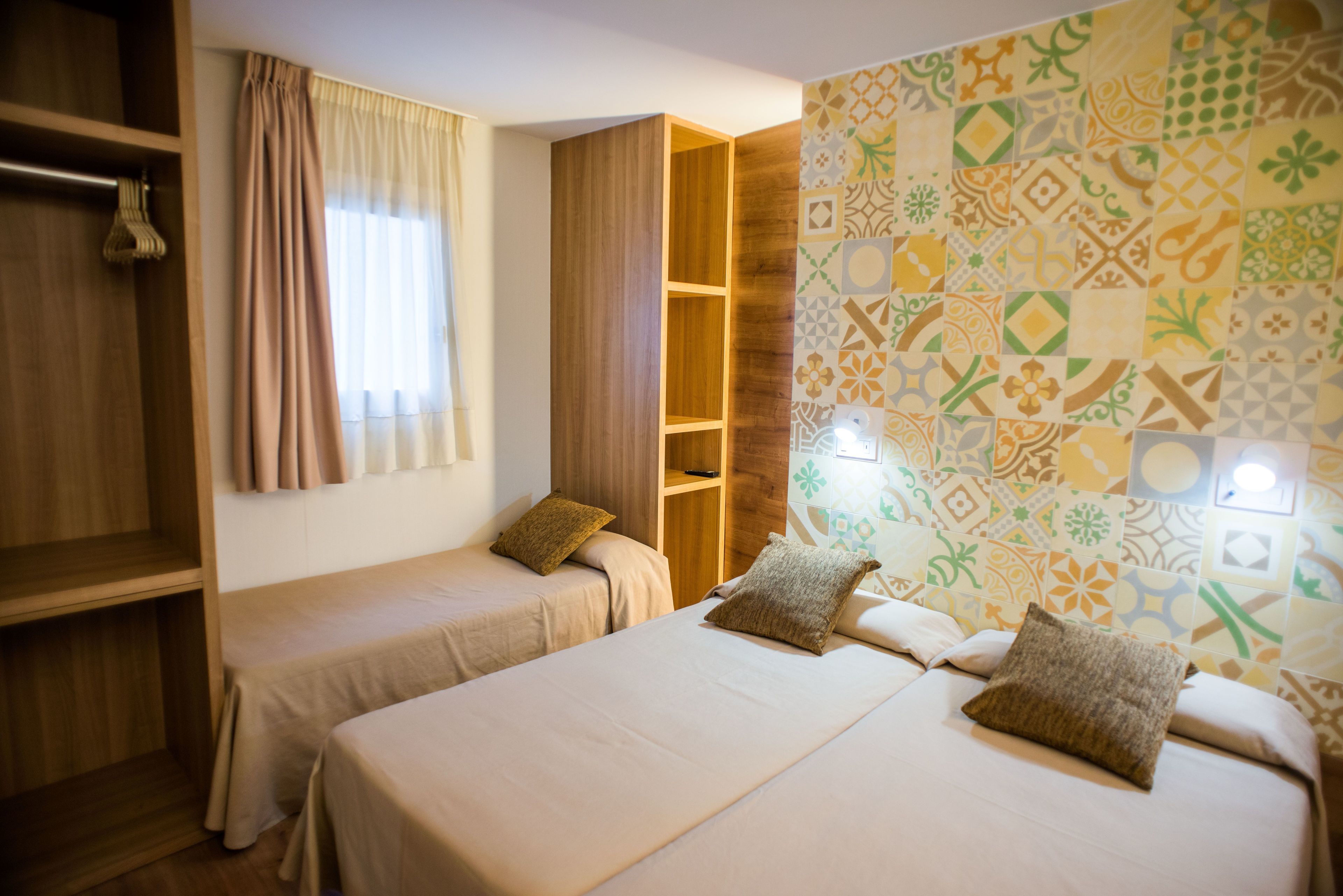 A hotel room with two beds, a wardrobe, and a patterned wall.