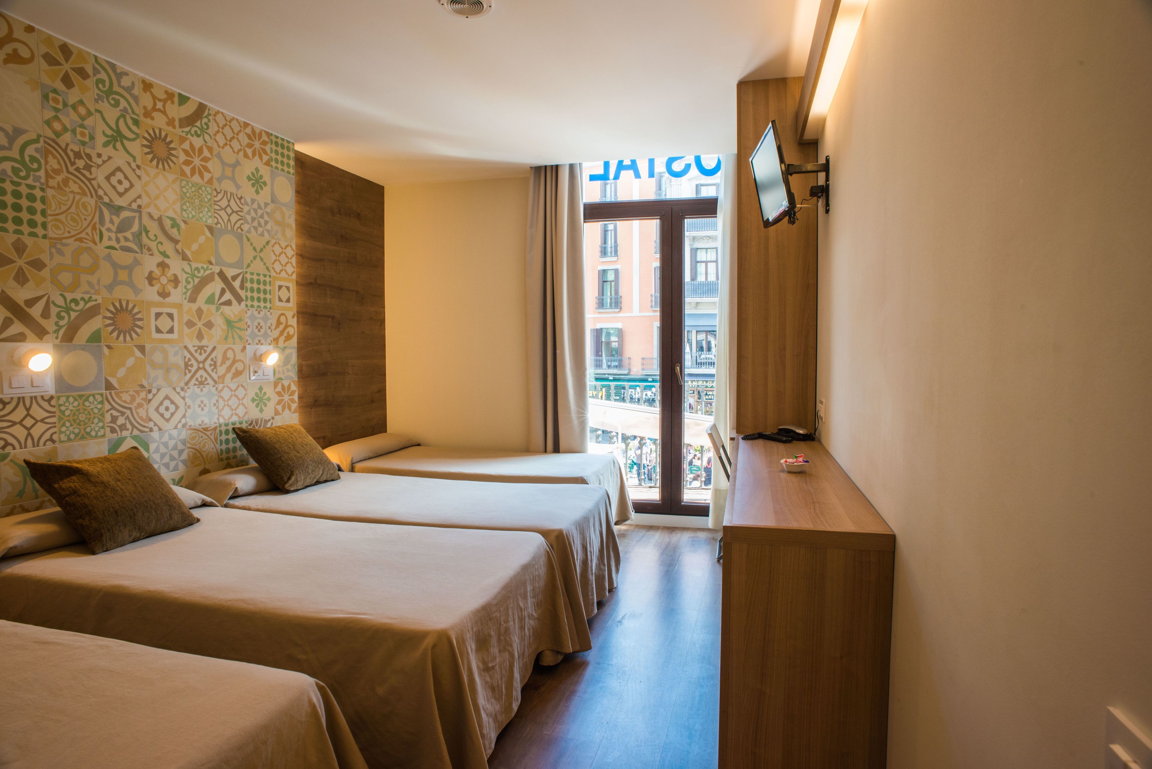 A hotel room with two beds, a wooden desk, a TV, and a patterned wall.