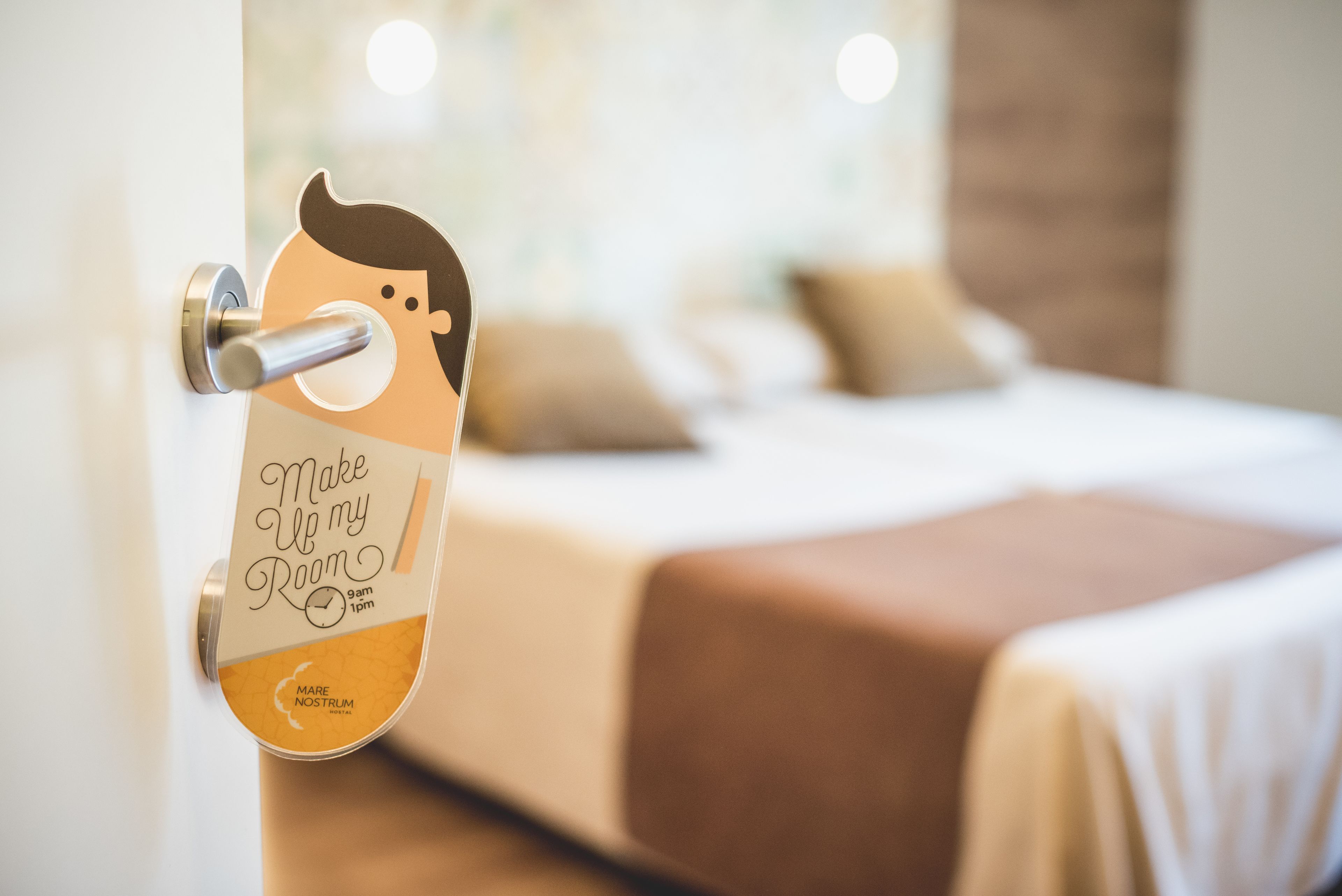 A hotel room with a bed, a door with a sign, and a window.