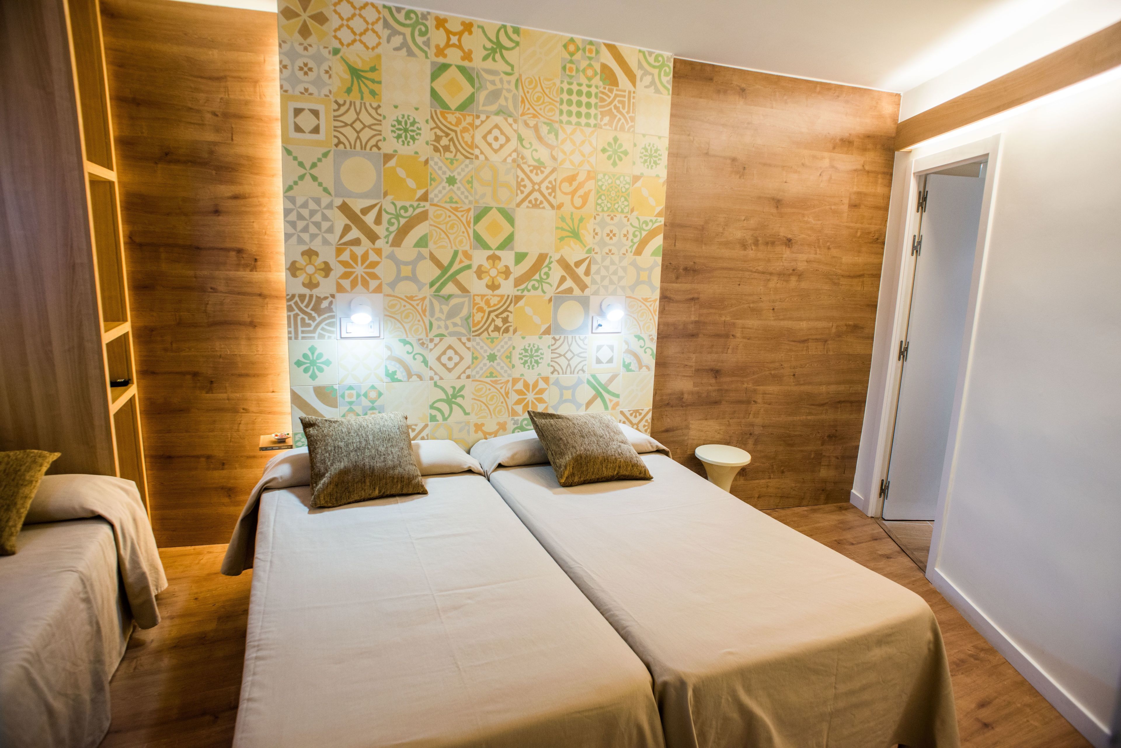 Habitación de hotel con dos camas, un papel tapiz estampado, suelo de madera y una puerta.