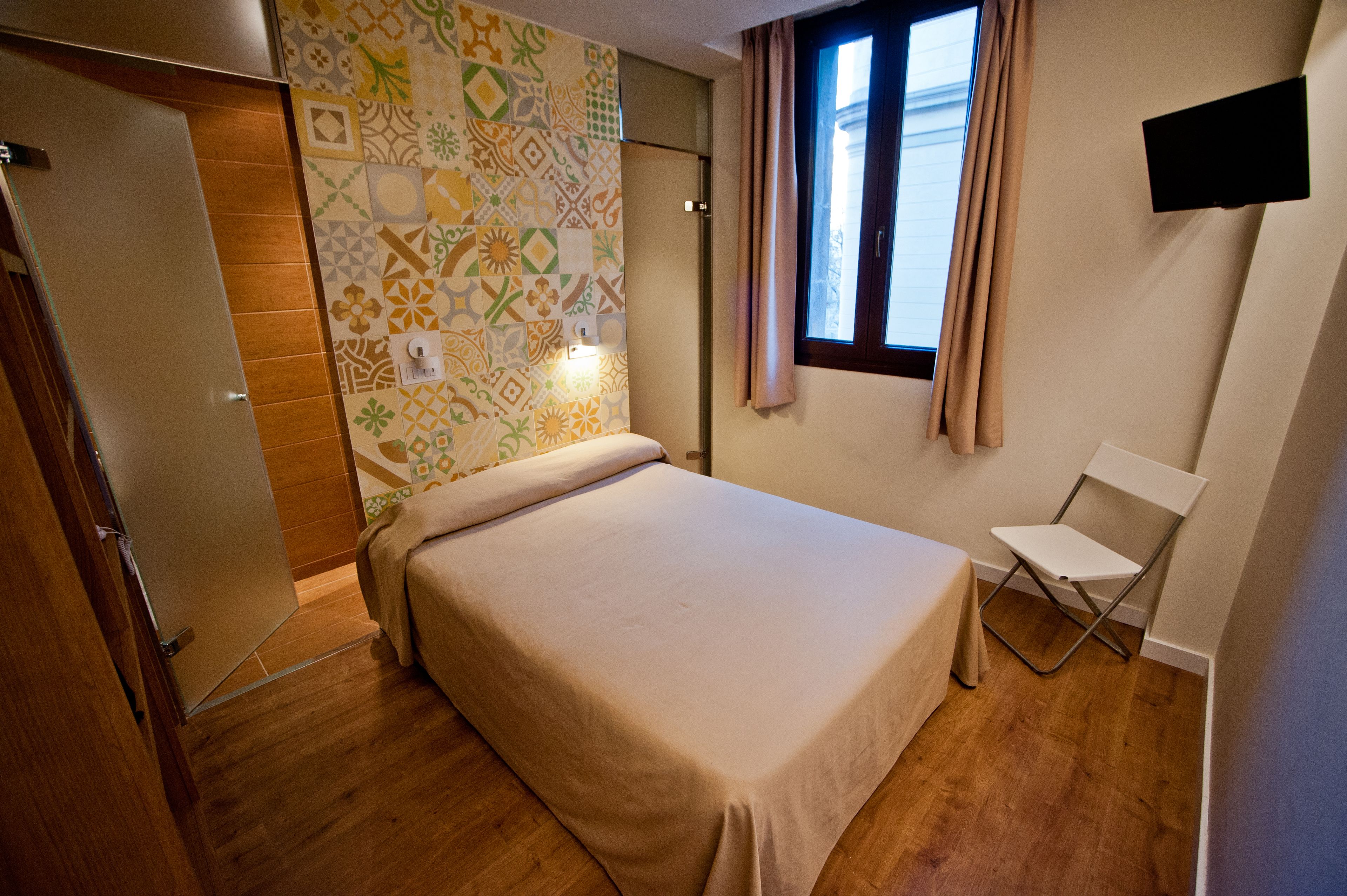 A bedroom with a bed, a chair, a TV, and a patterned wall.