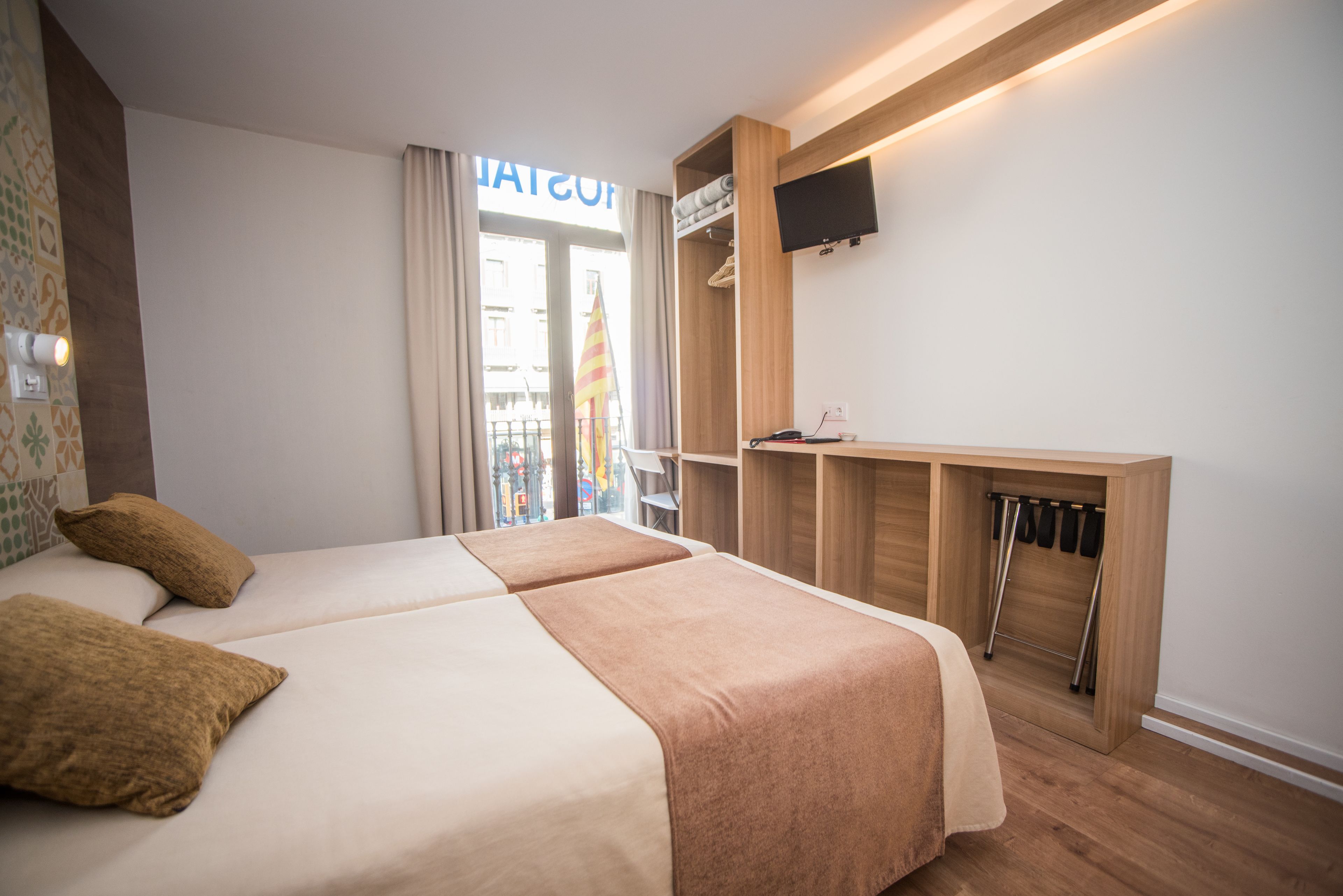 Une chambre d’hôtel avec deux lits, un téléviseur fixé au mur, un bureau en bois et une vue sur l’extérieur.