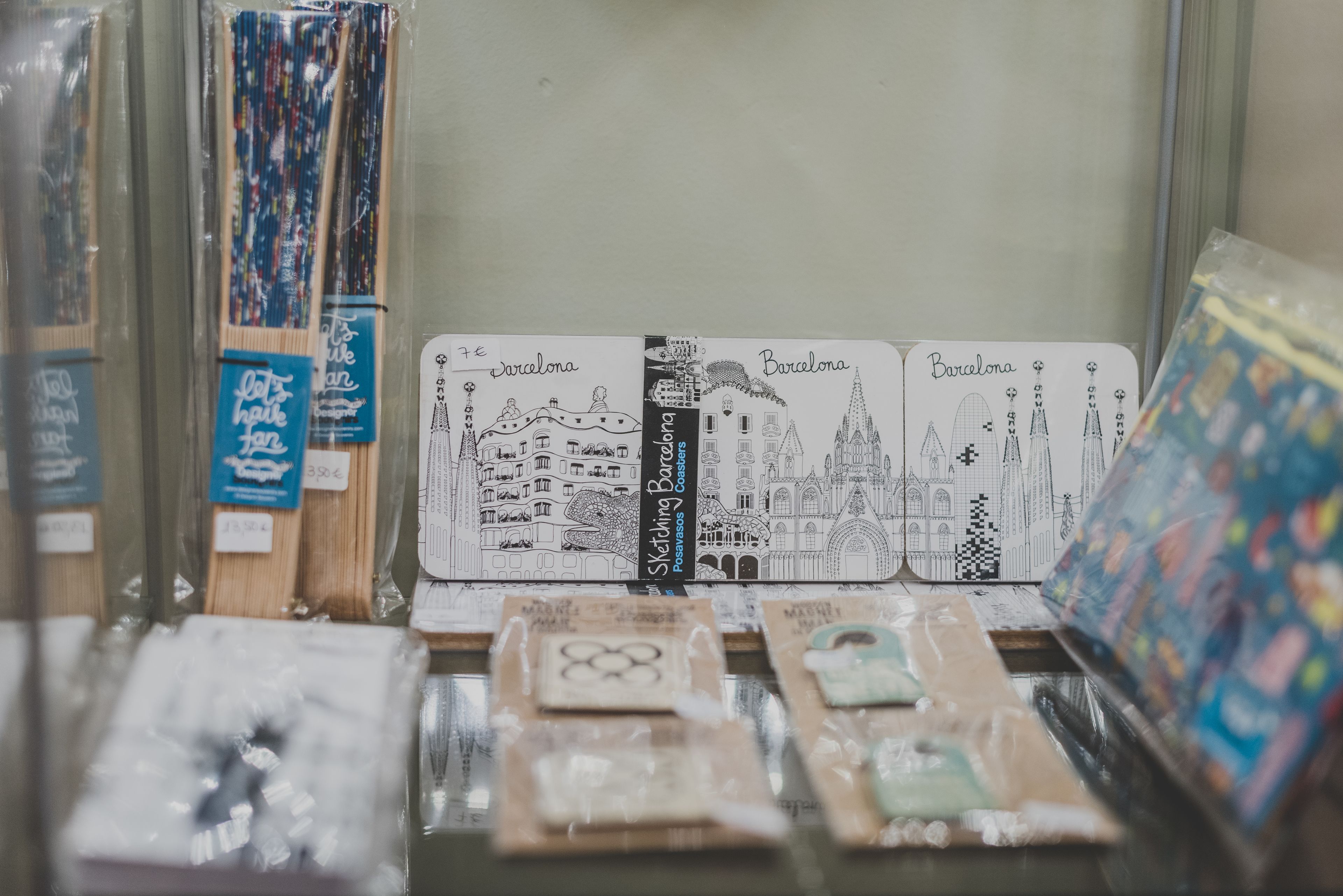Una exhibición de artículos de papelería con temática de Barcelona, incluyendo postales y cuadernos, con ilustraciones de los monumentos de la ciudad.