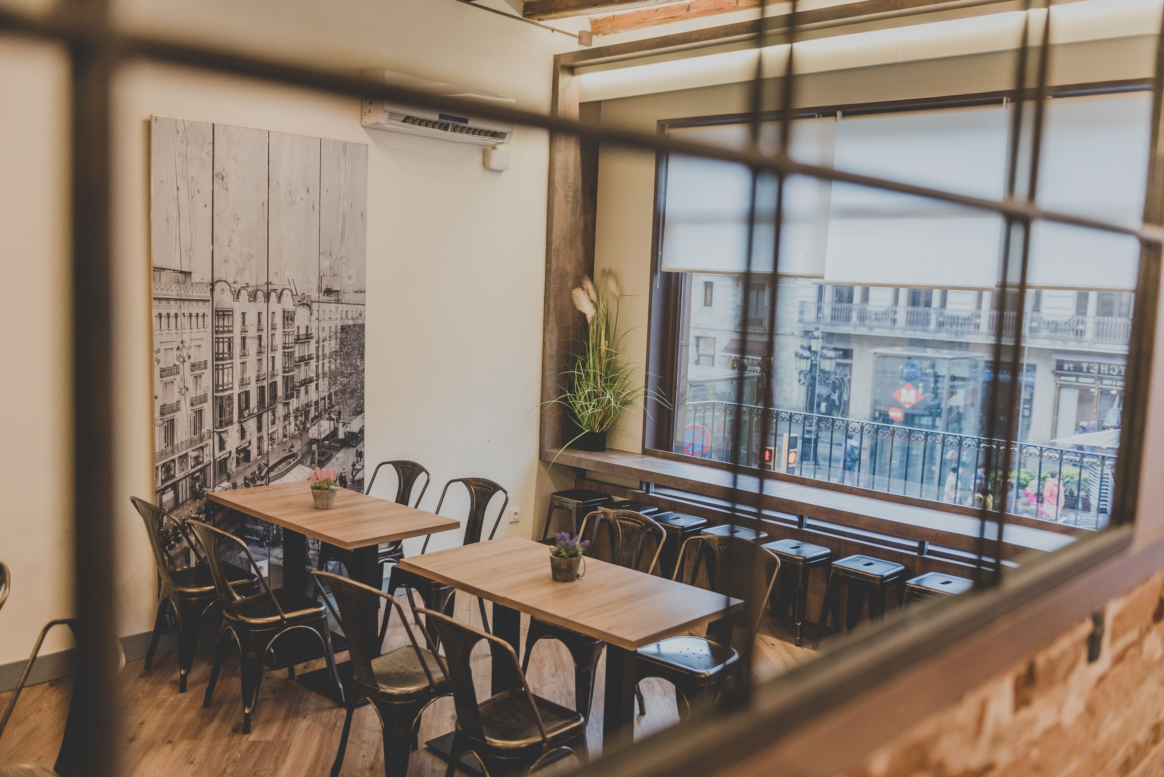 Un comedor con mesas y sillas de madera, un ventanal con vistas a la ciudad y un mural en blanco y negro en la pared.