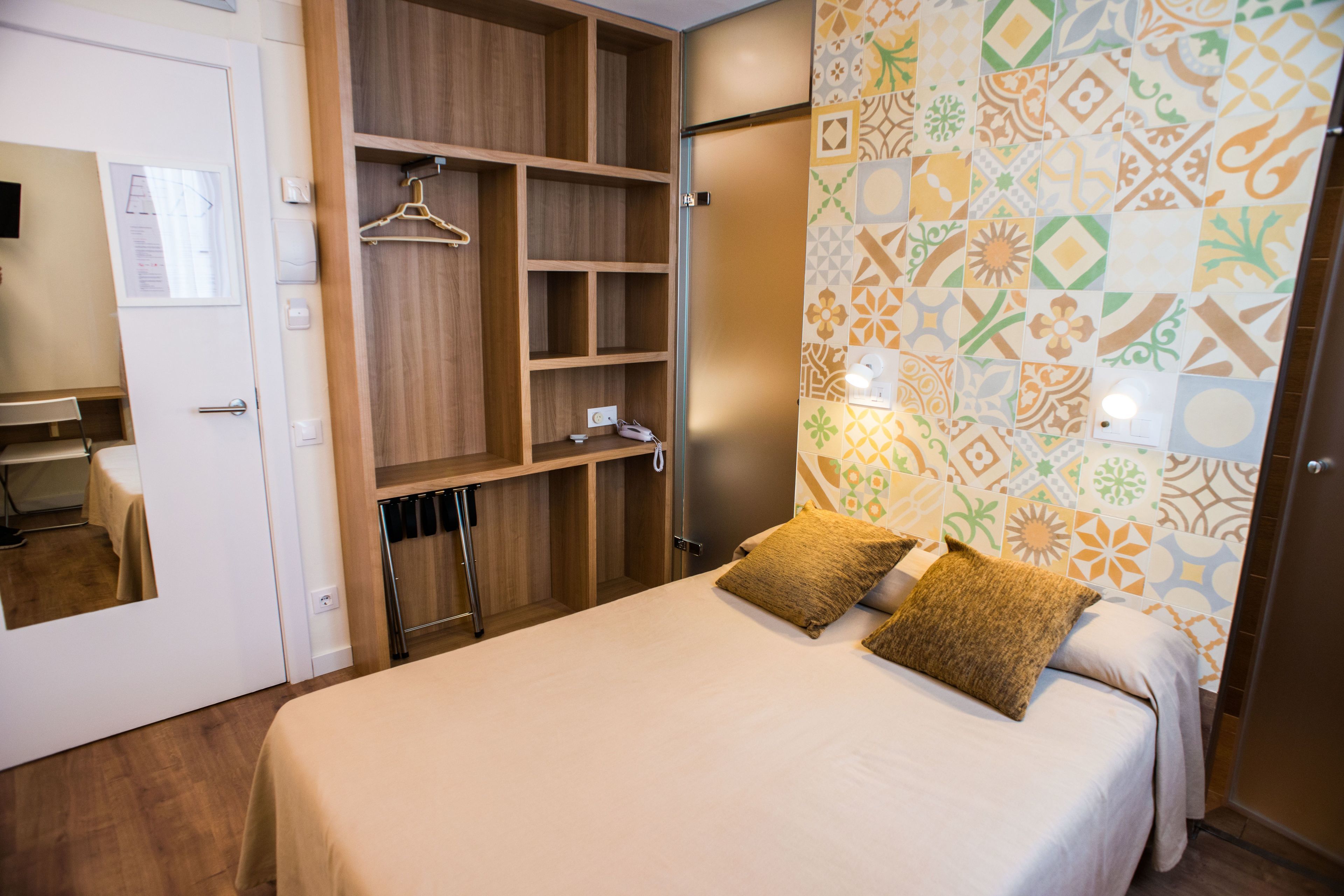 A hotel room with a bed, a wardrobe, a mirror, and a patterned wall.