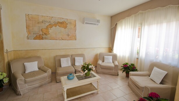 A living room with a beige sofa set, a coffee table with a vase of flowers, a map on the wall, and a window with sheer curtains.