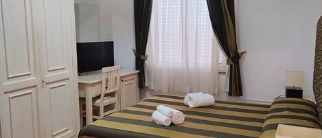 Habitación de hotel con cama, escritorio, armario, ventilador de techo y ventana con cortinas.