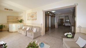 A living room with a beige sofa set, a cabinet with a map, and a dining area visible through an open doorway.