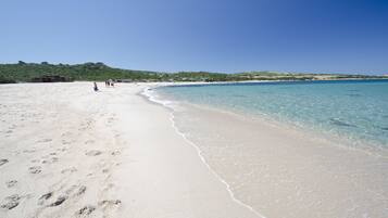 Ein sandiger Strand mit klarem, blauem Wasser und einer hügeligen Landschaft im Hintergrund.