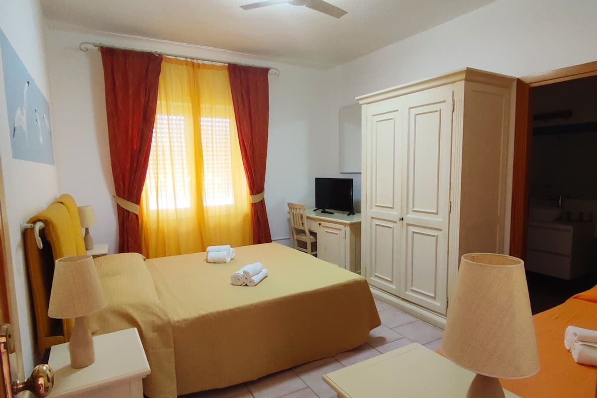 Une chambre d’hôtel comprenant un lit, deux tables de chevet avec lampes, un bureau avec une chaise, une télévision et une armoire.