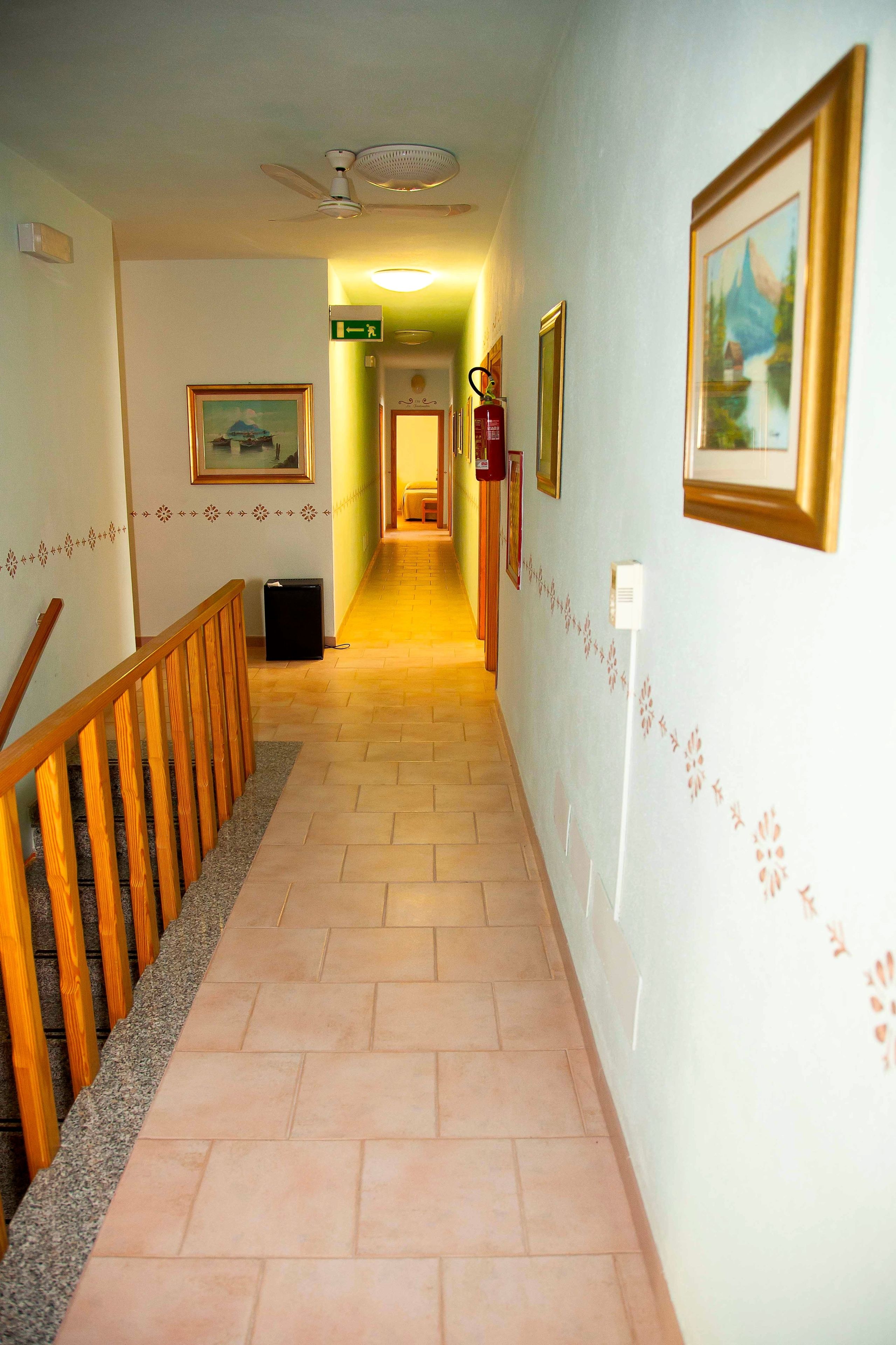 A hallway with a wooden railing, tiled floor, and framed pictures on the walls.