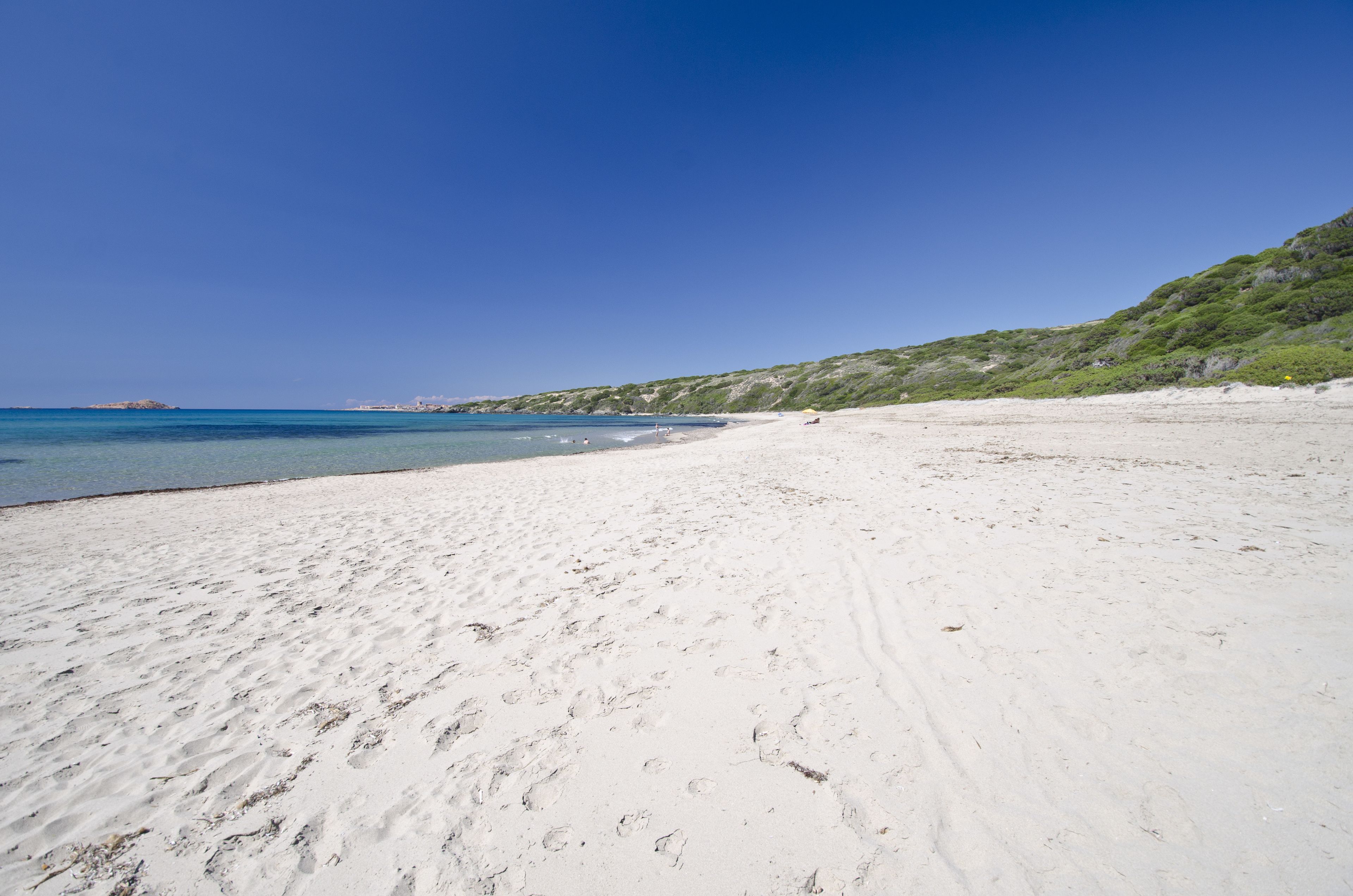 A wide sandy beach with clear blue water and a distant shoreline.