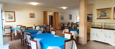 Un comedor con varias mesas y sillas, un armario blanco con objetos decorativos y obras de arte enmarcadas en las paredes.